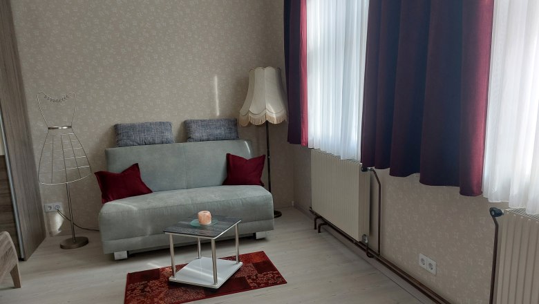 Ob&yacute;vacia izba so sivou pohovkou, červen&yacute;mi vank&uacute;&scaron;mi, stojacou lampou a stol&iacute;kom na červenom koberci.