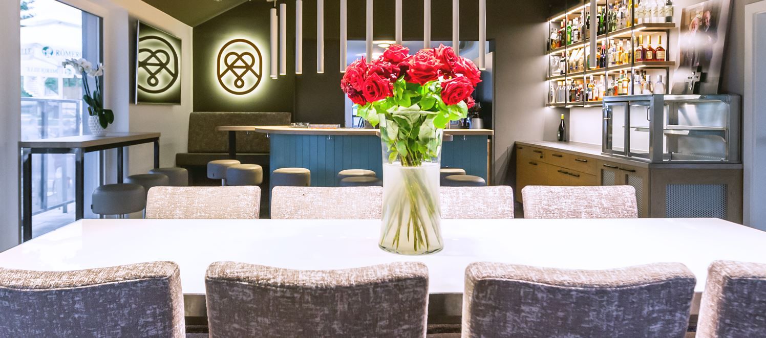 Pohľad do interiéru modernej reštaurácie s drevenými stolmi a policami; teplé osvetlenie a útulná atmosféra na vychutnávanie a ochutnávanie.