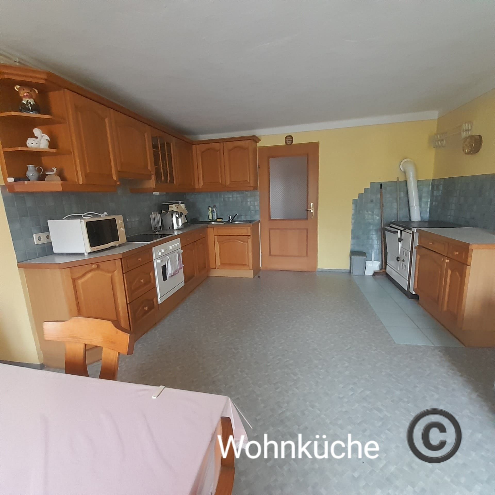 Priestranná kuchyňa s dreveným nábytkom, jedálenským stolom, sporákom, mikrovlnnou rúrou a žltými stenami.