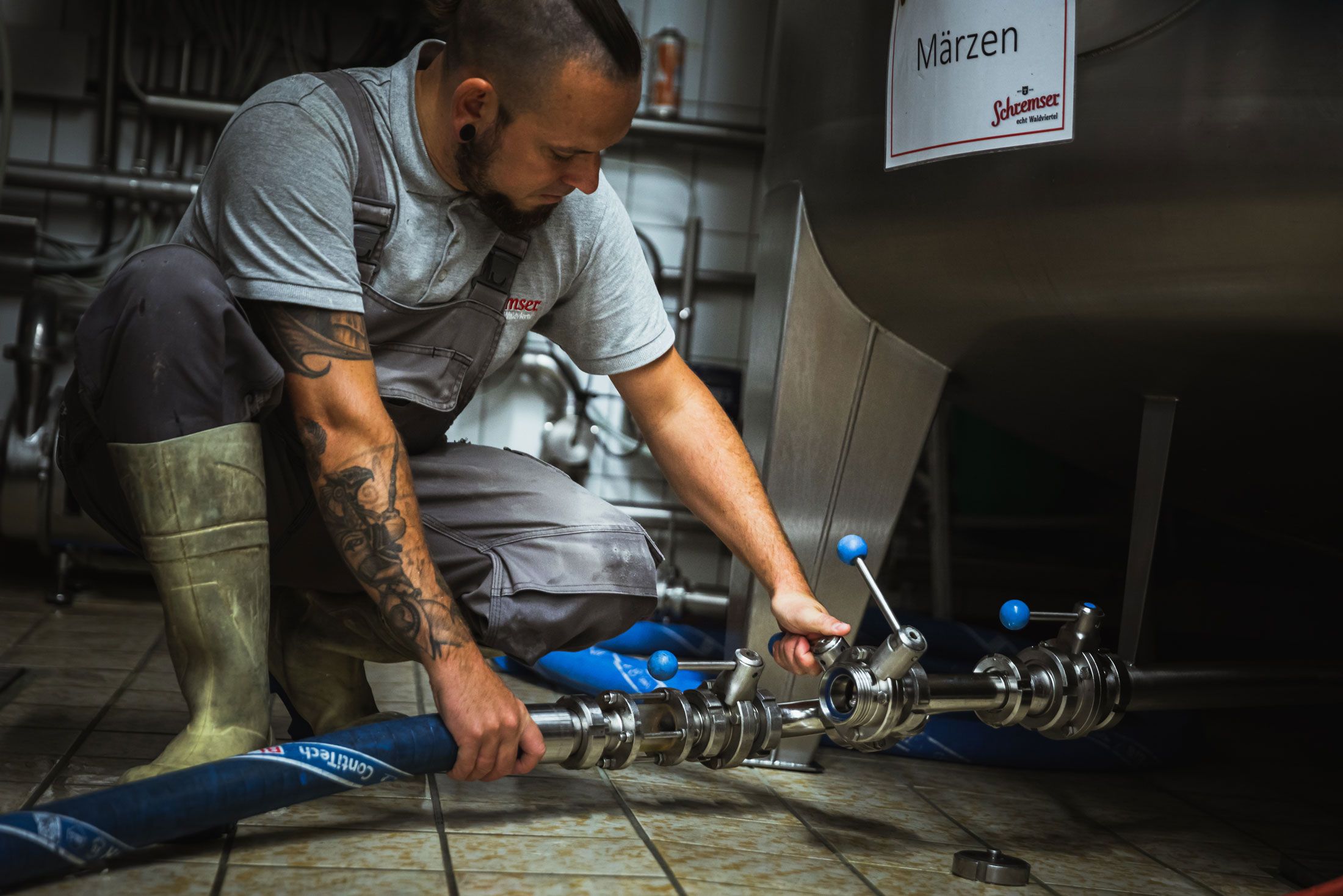 Muž v pracovnom odeve drží poháre s pivom pred pivovarom.