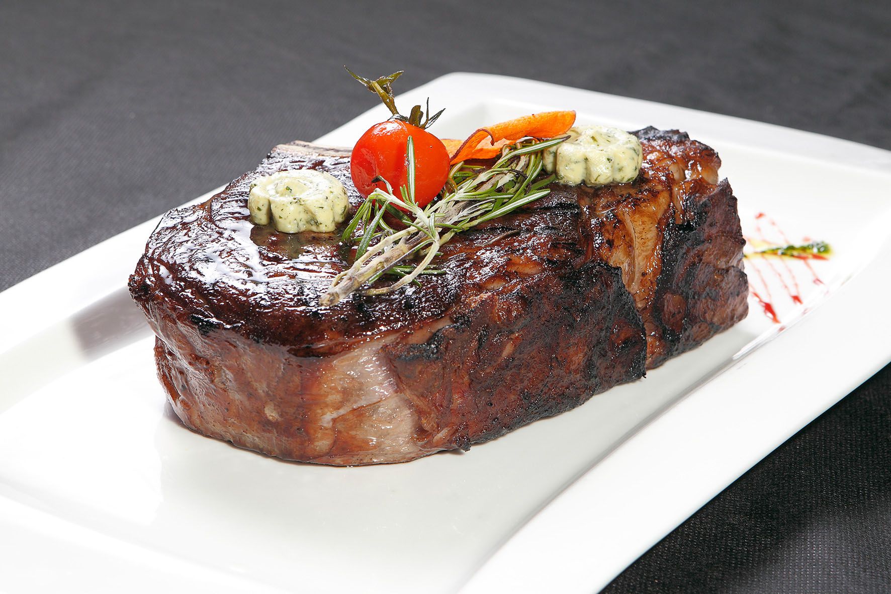 Šťavnatý steak s bylinkovým maslom, rozmarínom a cherry paradajkou na bielom tanieri.
