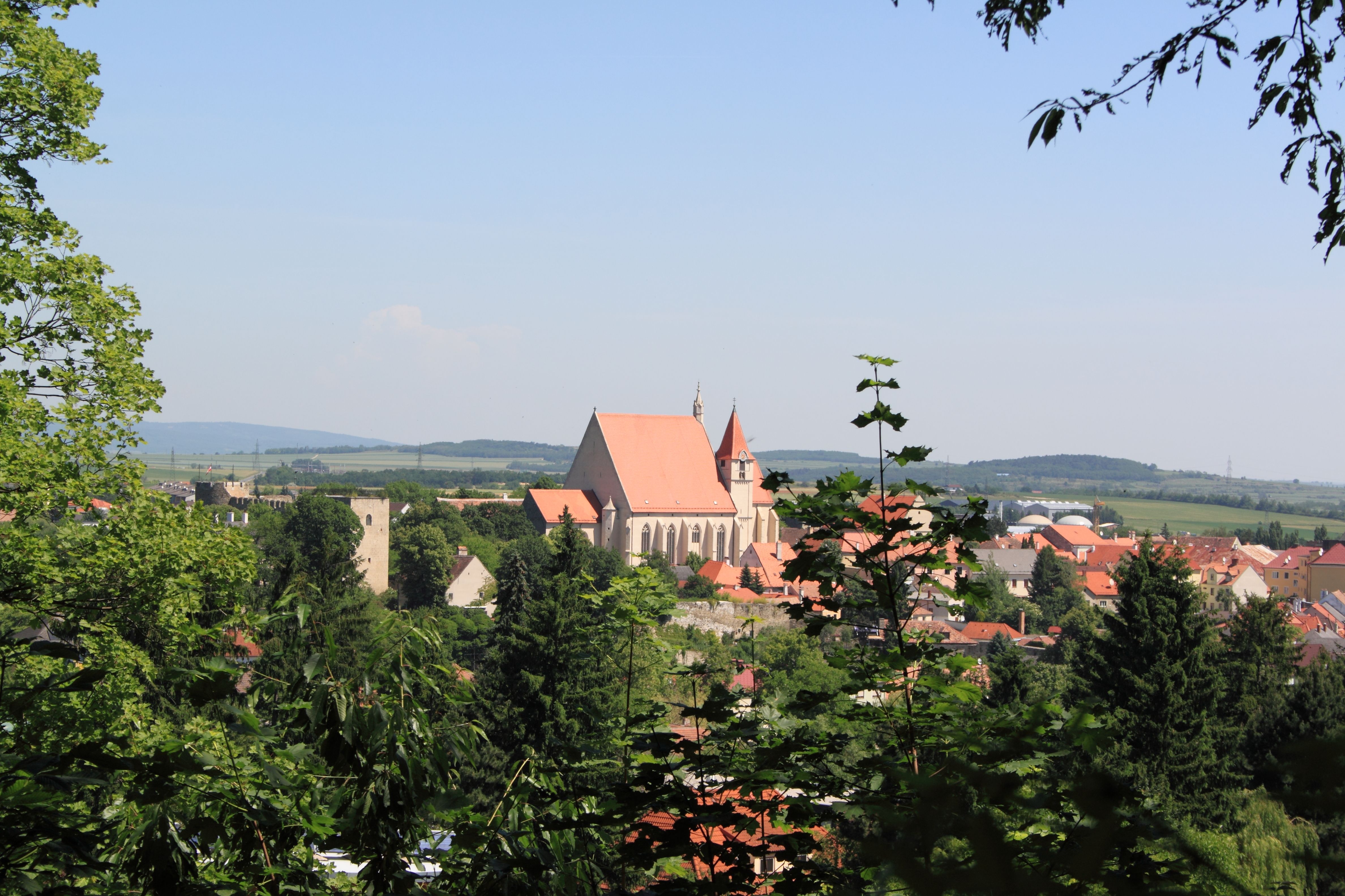 Panoramatický pohľad na Eggenburg s kostolom a okolitými budovami, v pozadí obklopený stromami a kopcami.