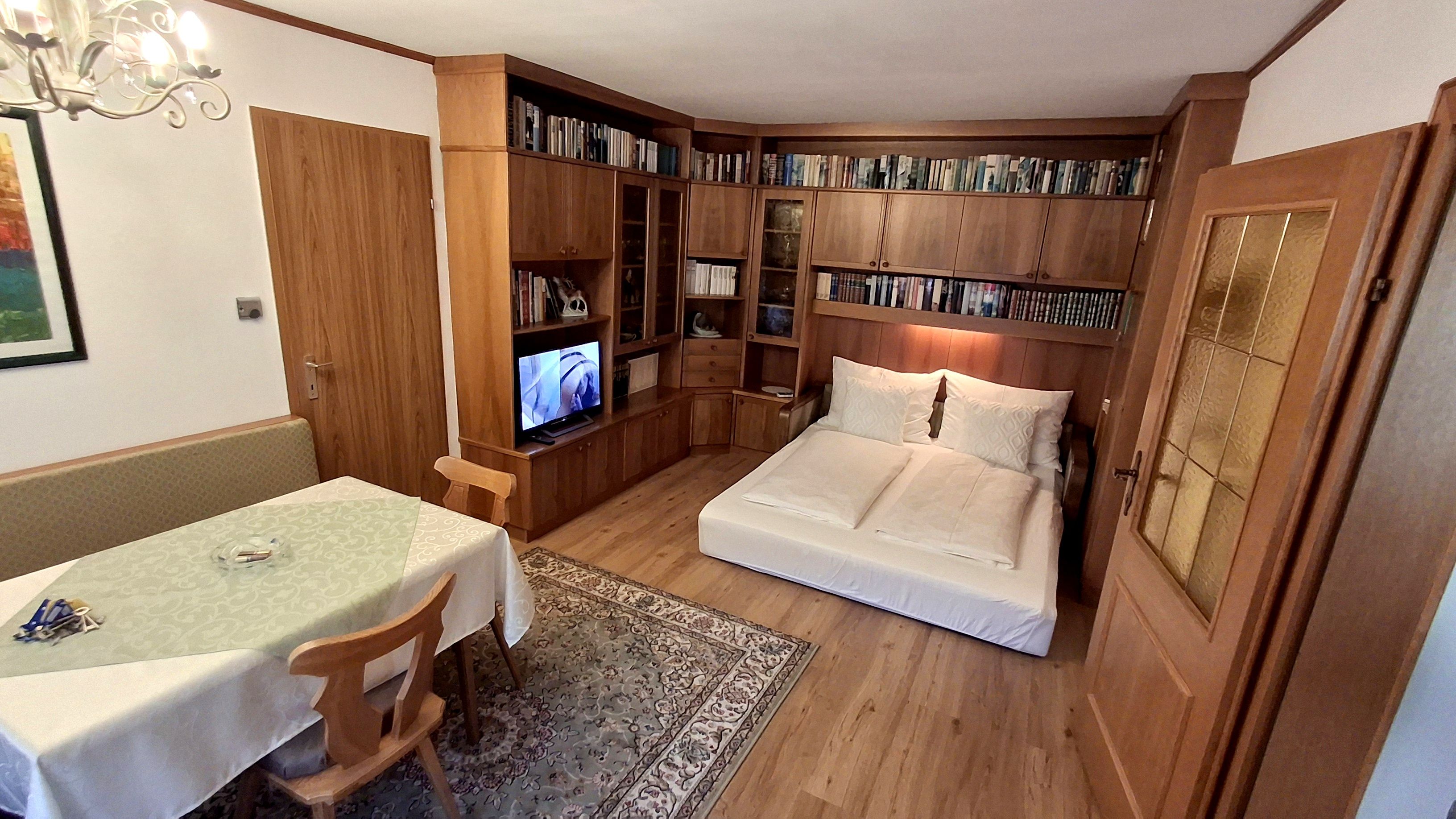 Obývacia izba s rozkladacou pohovkou, policou na knihy, jedálenským stolom a TV.