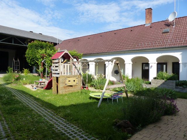 Vnútorný dvor s detským ihriskom, obklopený budovou s červenými škridlami a bielymi stenami.