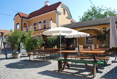 Útulný dvor s drevenými stolmi a lavicami pred žltou budovou.