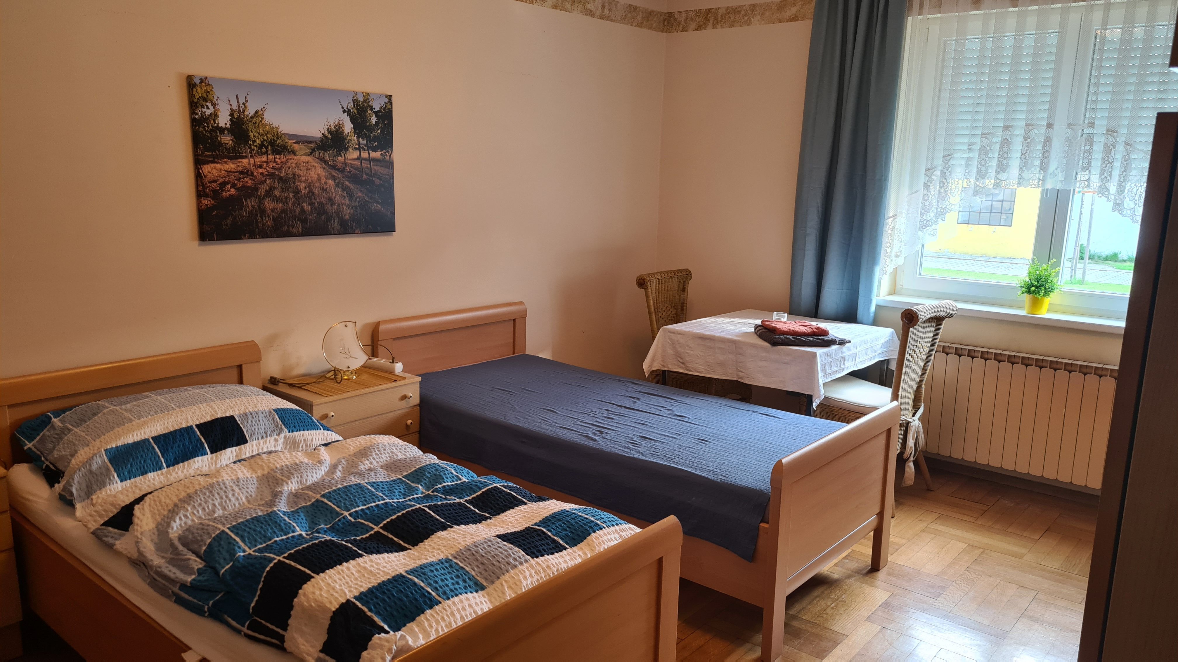 Jednoducho zariadená spálňa s dvoma samostatnými posteľami, stolom a stoličkou a oknom so závesmi.