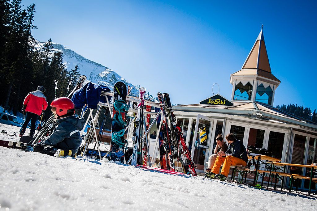 Lyžiari pred barom JoSchi s lyžami a snowboardami na snehu.