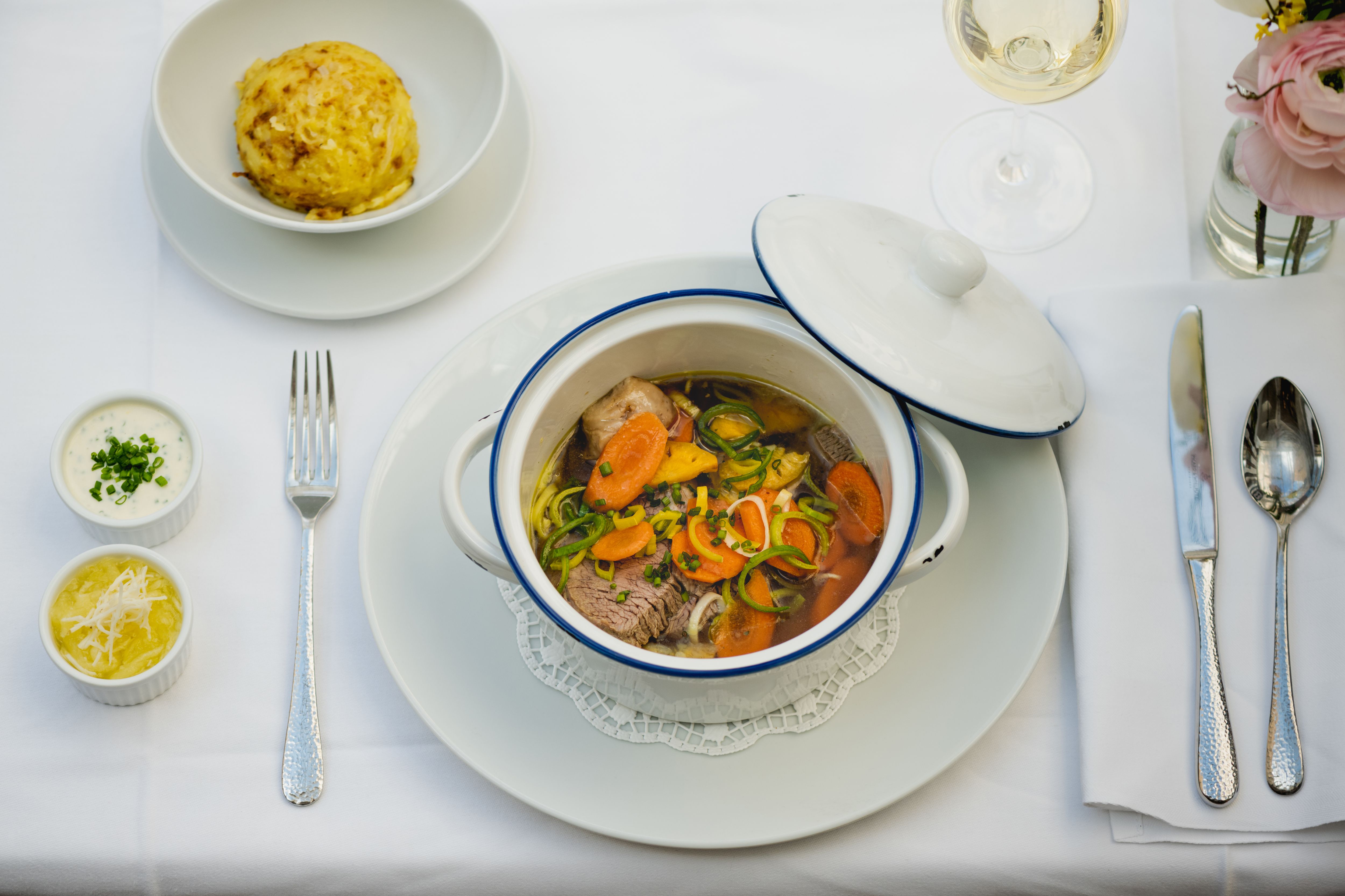 Stôl prestretý gulášom v bielom hrnci, knedľou, dvoma omáčkami a pohárom bieleho vína.