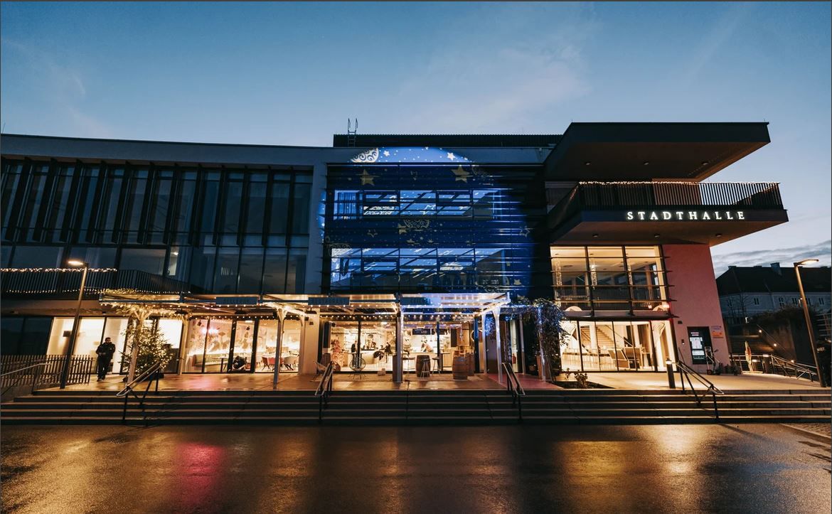 Exteriérový pohľad na Stadthalle Ybbs za súmraku s osvetleným vchodom.