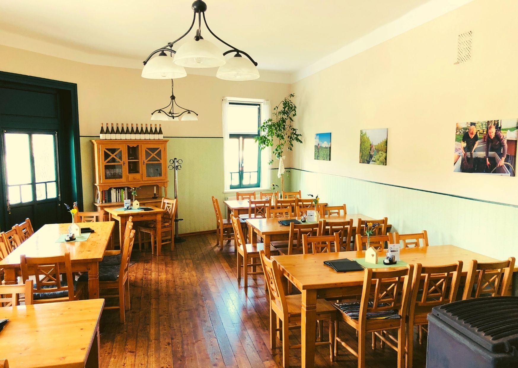 Útulná jedáleň s drevenými stolmi a stoličkami, ozdobená fľašami vína a obrázkami na stene.