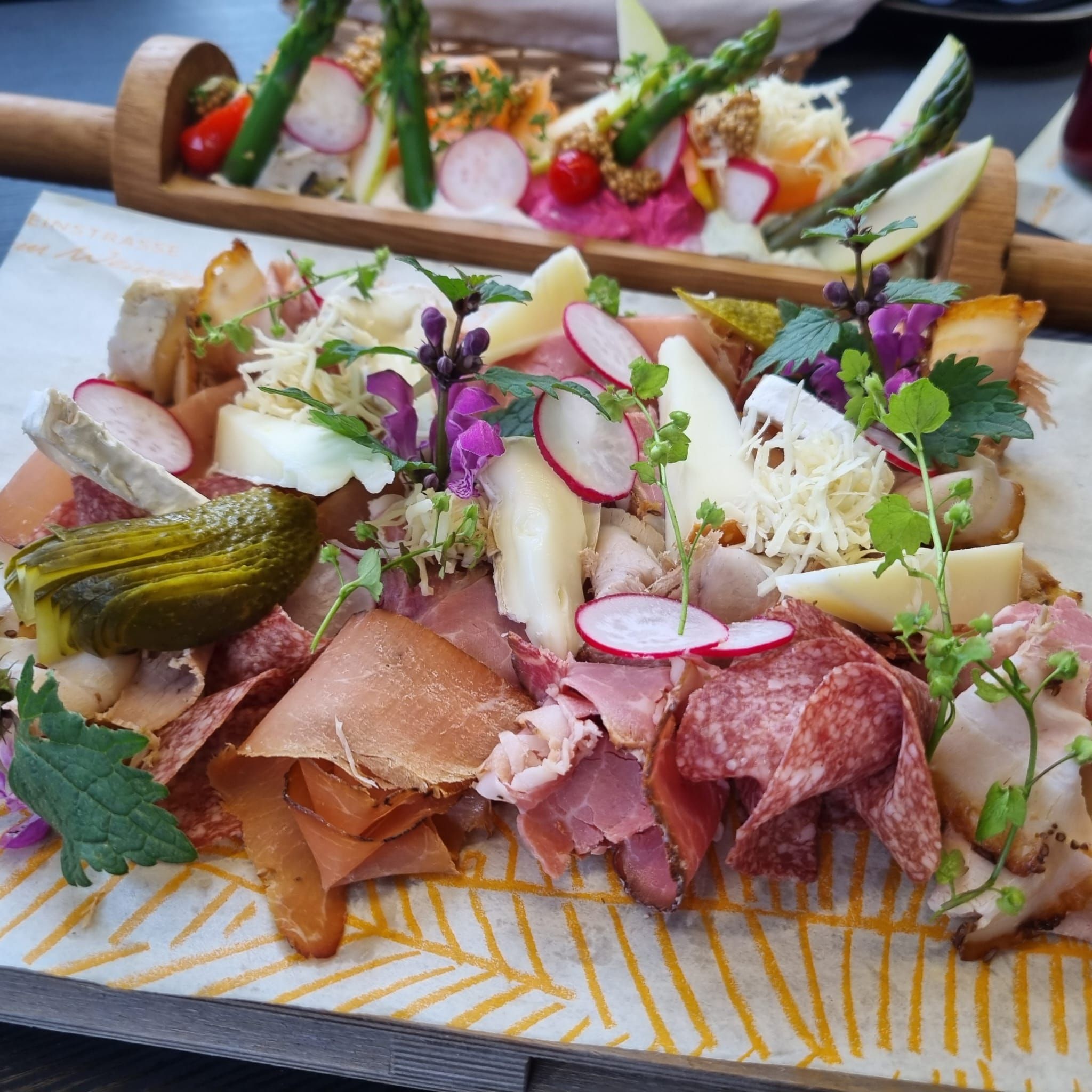 Heurigen tanier s rôznymi druhmi klobás a syrov, reďkovkami, uhorkami a bylinkami podávaný na drevenej doske.