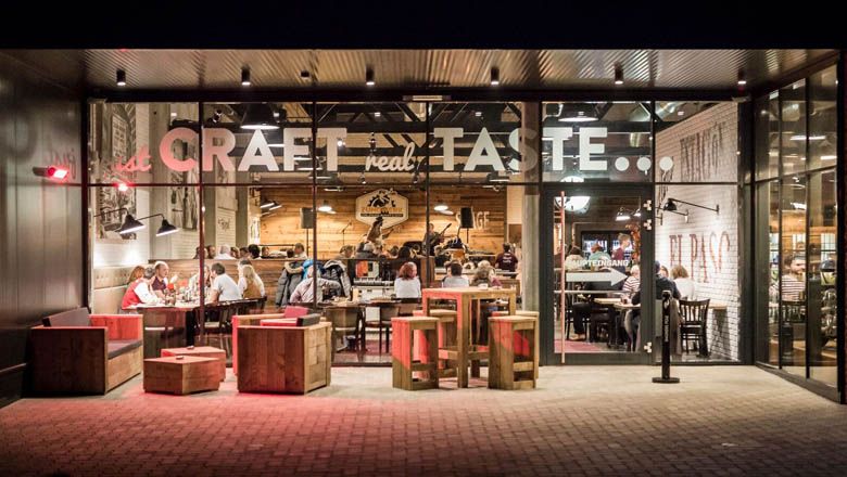 Exteriérový pohľad na reštauráciu s preskleným priečelím a dreveným nábytkom.