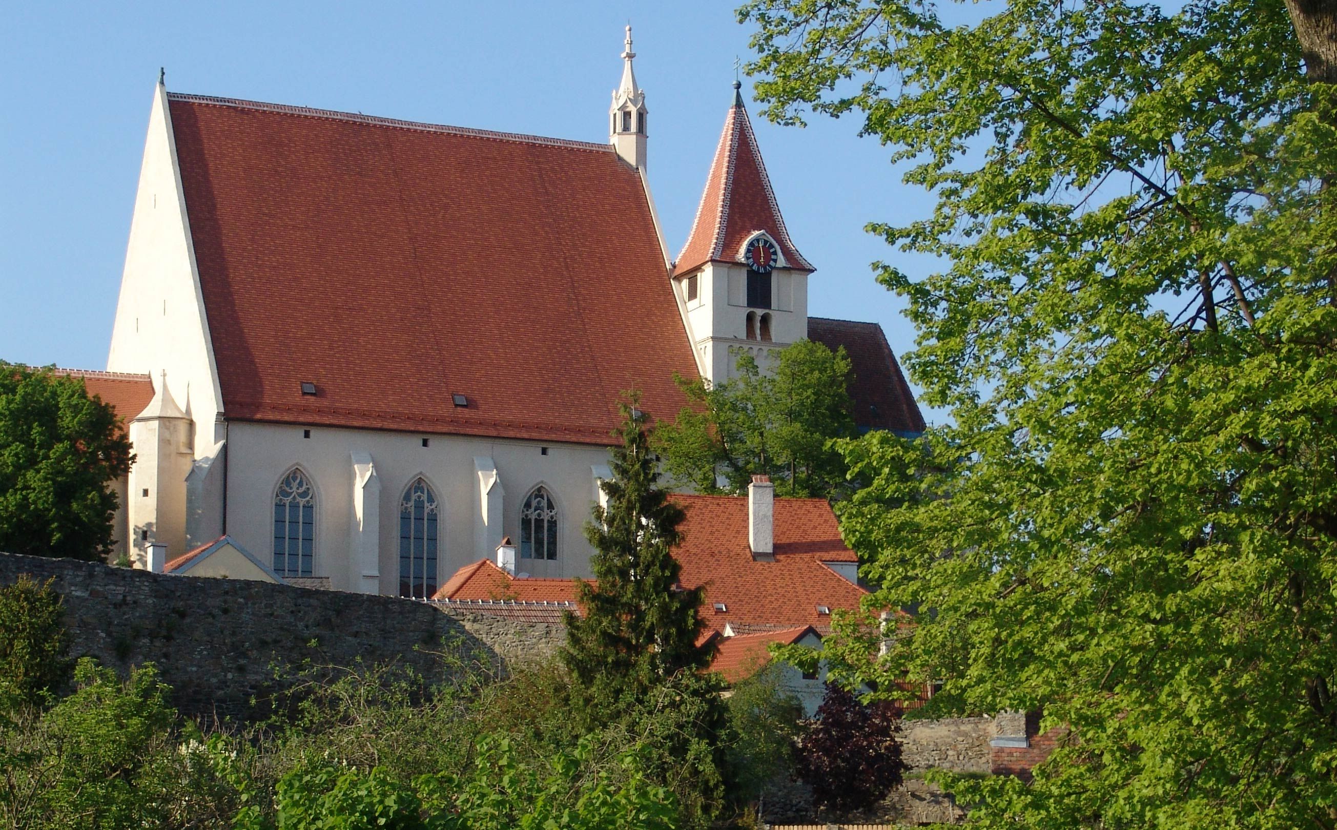 Štefana s červenou strechou a vežou, obklopený stromami a kamenným múrom.