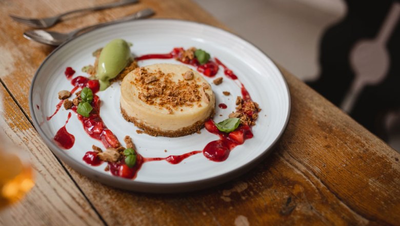 Tanier s tvarohovým koláčom zdobeným červenými bobuľami a zelenou zmrzlinou na drevenom stole.