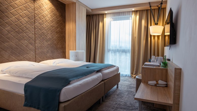 Alfred, © Niederösterreich Werbung / Maximilian Pawlikowsky Moderná hotelová izba s manželskou posteľou, dreveným obložením a oknami so závesmi.