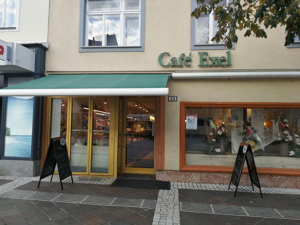 Exteriérový pohľad na kaviareň Café Exel so zelenou markízou a výzdobou výkladu.