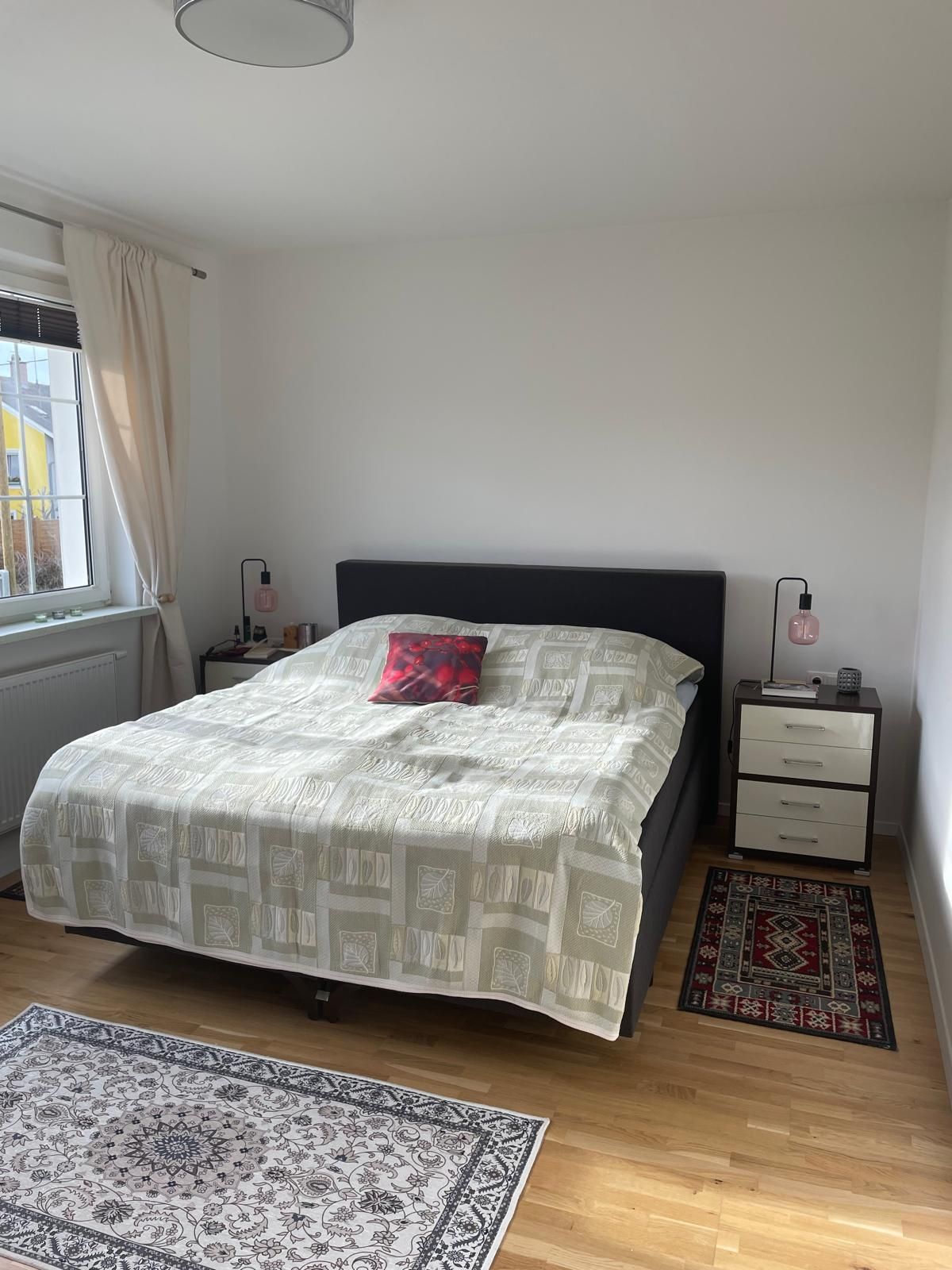 Jedna spálňa s manželskou posteľou, dvoma nočnými stolíkmi a kobercami na drevenej podlahe.