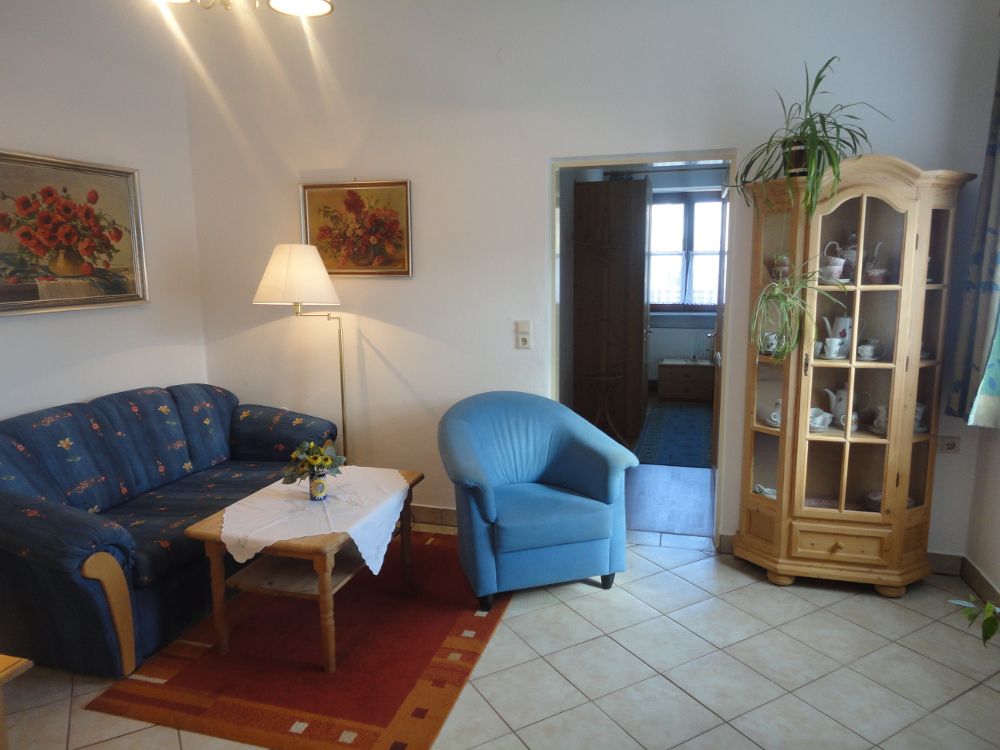 Obývacia izba s modrou pohovkou, modrým kreslom, dreveným stolom a vitrínou.