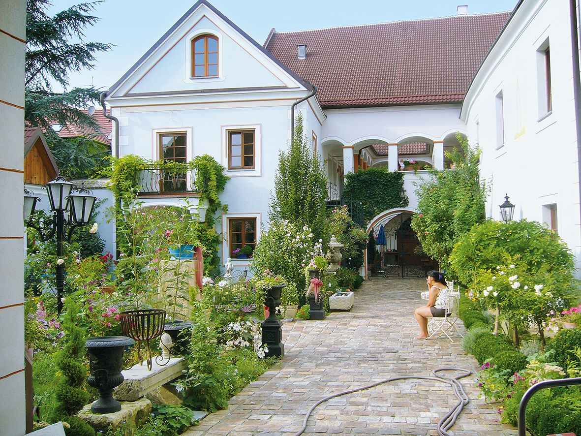 Idylické nádvorie s rastlinami a sediacou osobou.