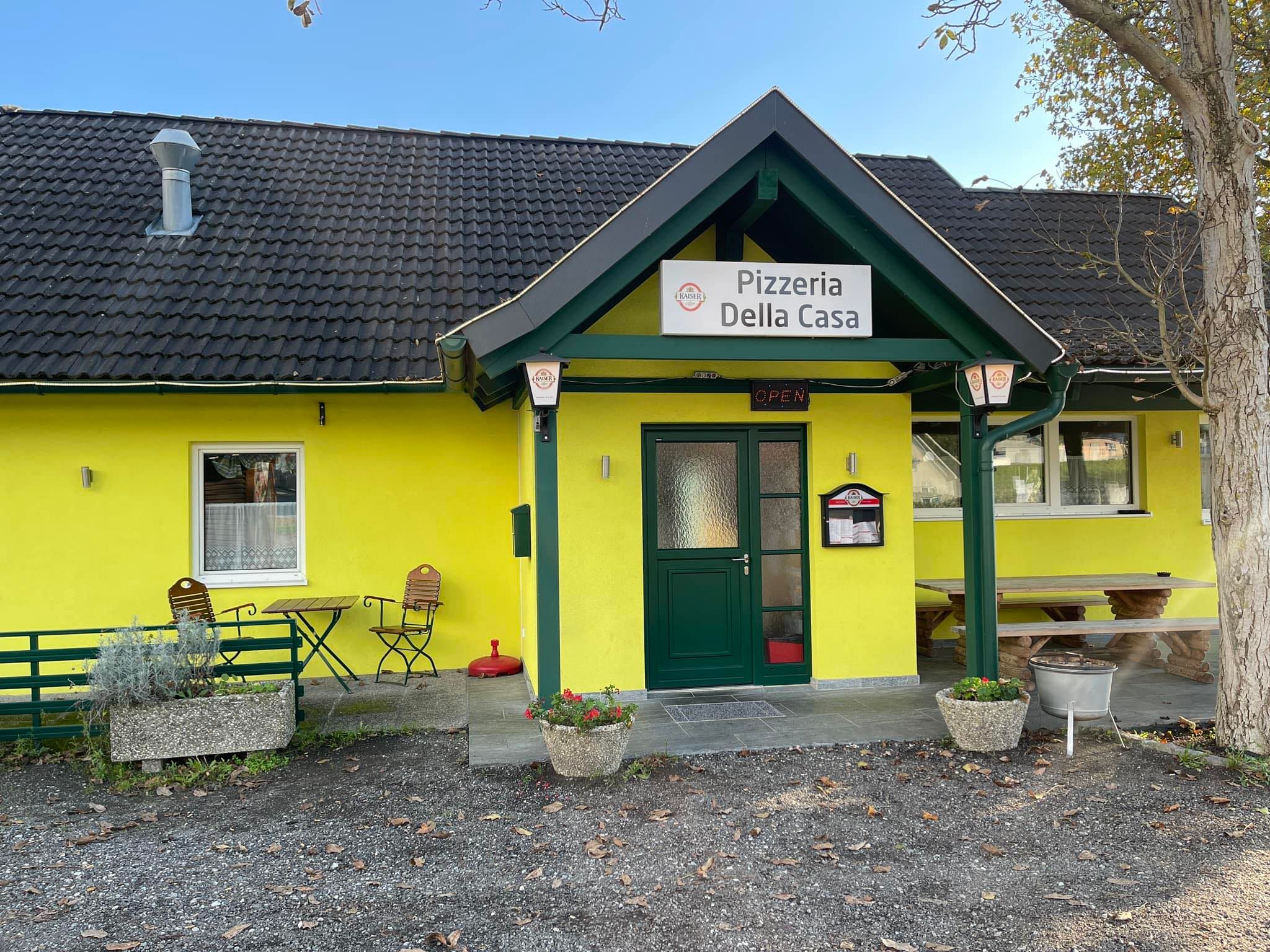 Pohľad na žltú pizzeriu s názvom "Pizzeria Della Casa" zvonku.