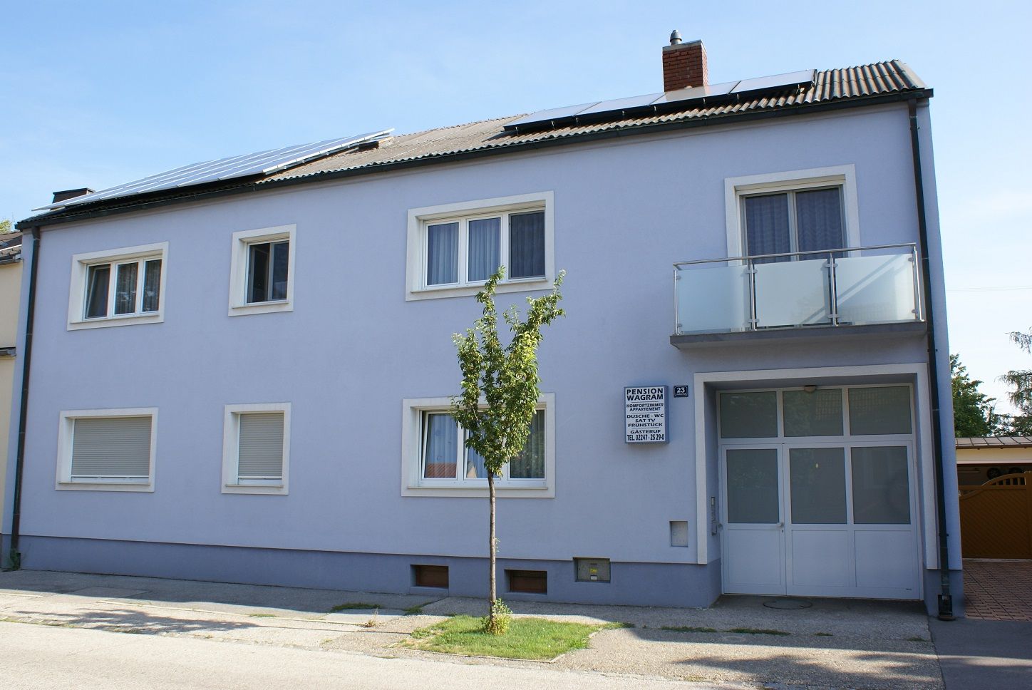 Pohľad zvonku na dvojpodlažnú budovu s modrou fasádou a solárnymi panelmi na streche.