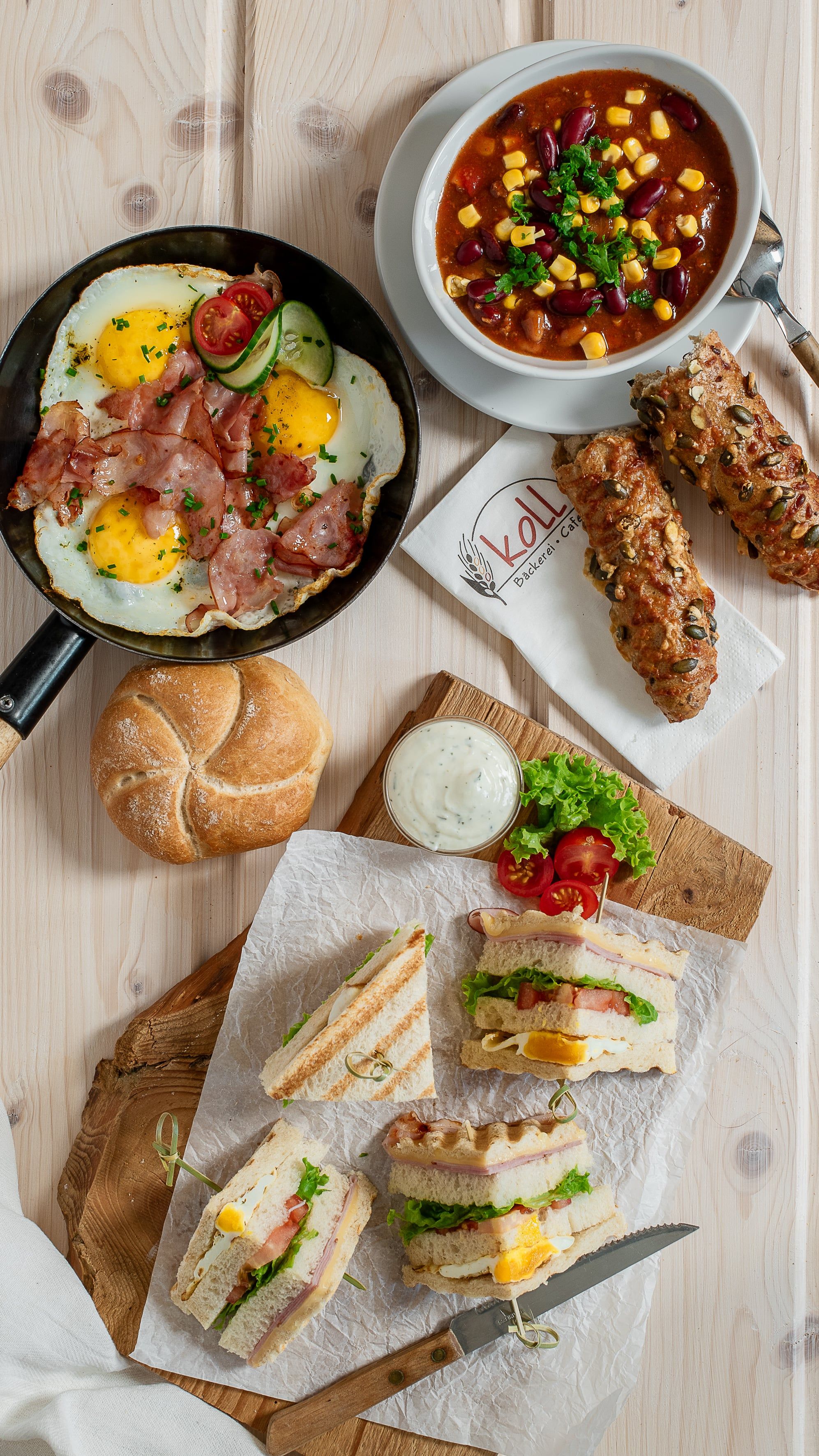 Rôzne teplé občerstvenie na stole vrátane vyprážaných vajec so slaninou, polievky, sendvičov a žemlí.