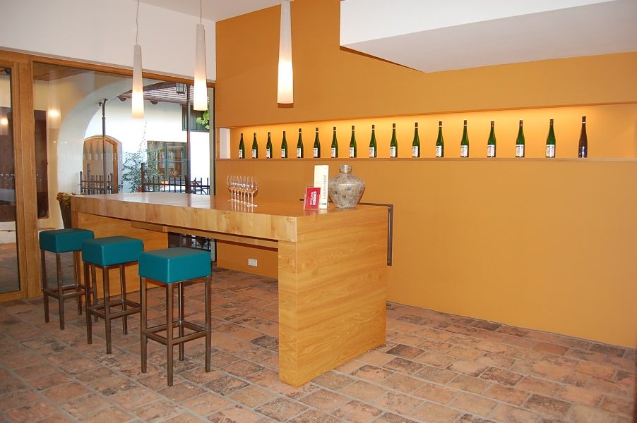 Moderná degustačná miestnosť s dreveným pultom, barovými stoličkami a fľašami vína na stene.