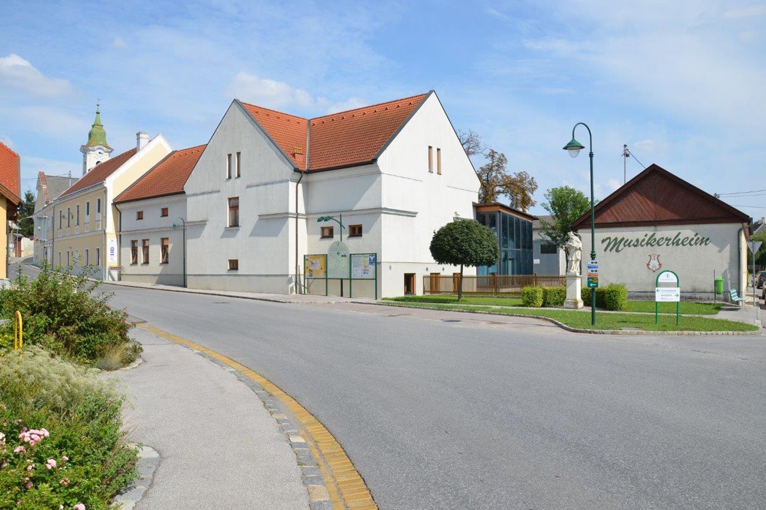 Scéna z ulice v Hohenruppersdorfe s domom hudobníkov a kostolom v pozadí.