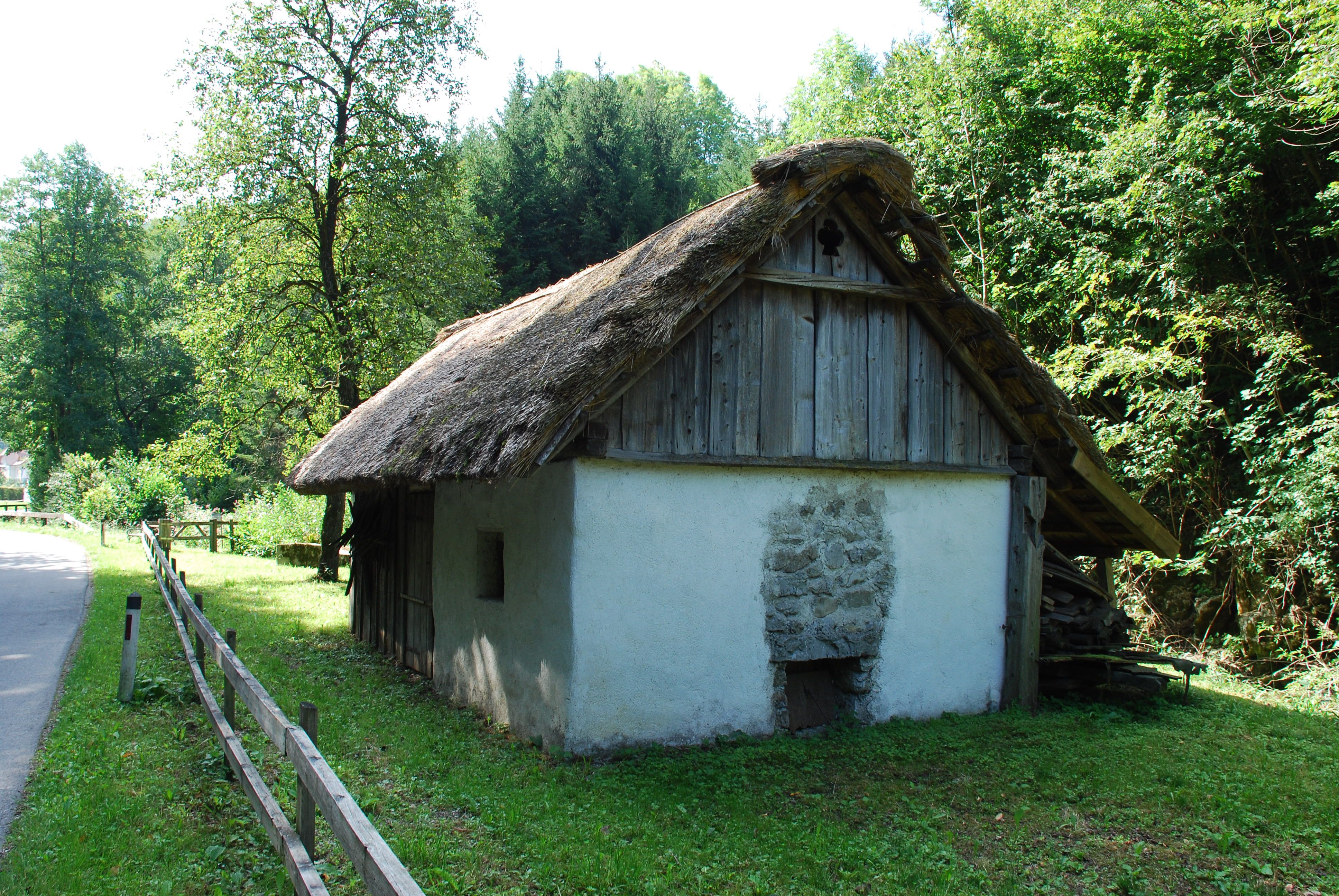 Tradičná slamená chata vo vidieckom prostredí, obklopená stromami a lúkami.