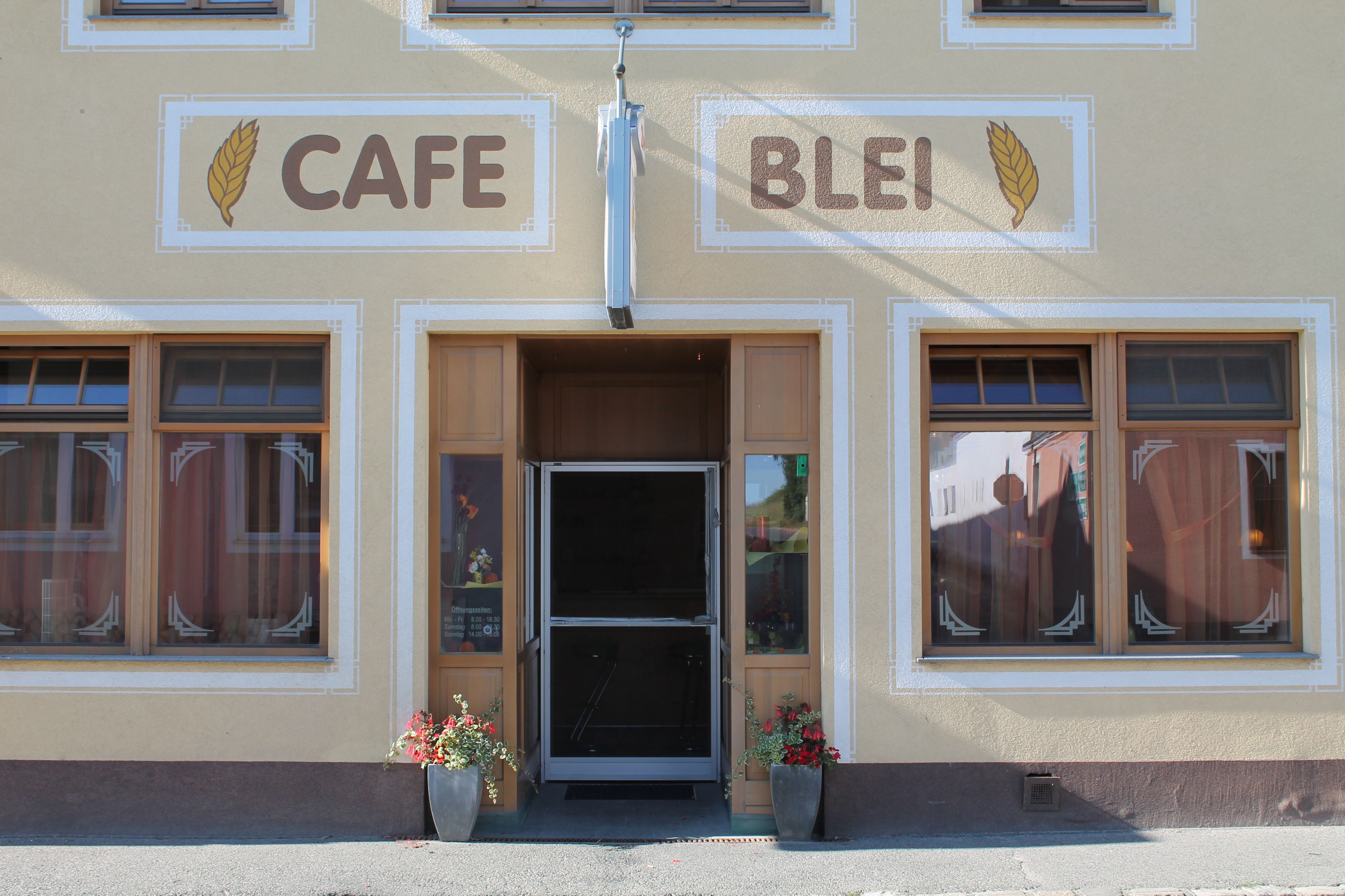 Vchod do kaviarne s nápisom "Cafe Blei" a kvetinovou výzdobou.