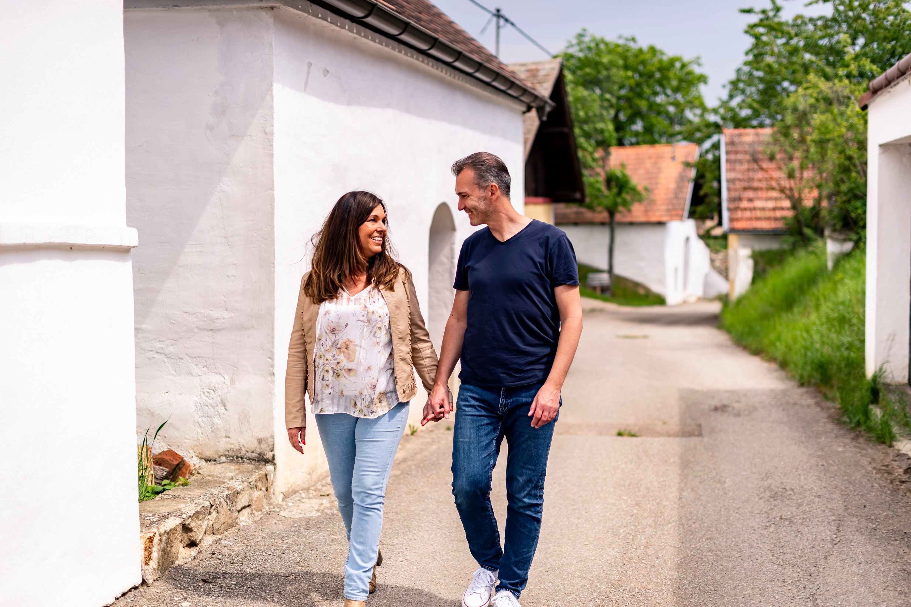 Dvojica sa ruka v ruke prechádza po ulici Öhlbergkellergasse v Pillersdorfe, obklopená tradičnými vínnymi pivnicami a zelenou krajinou.