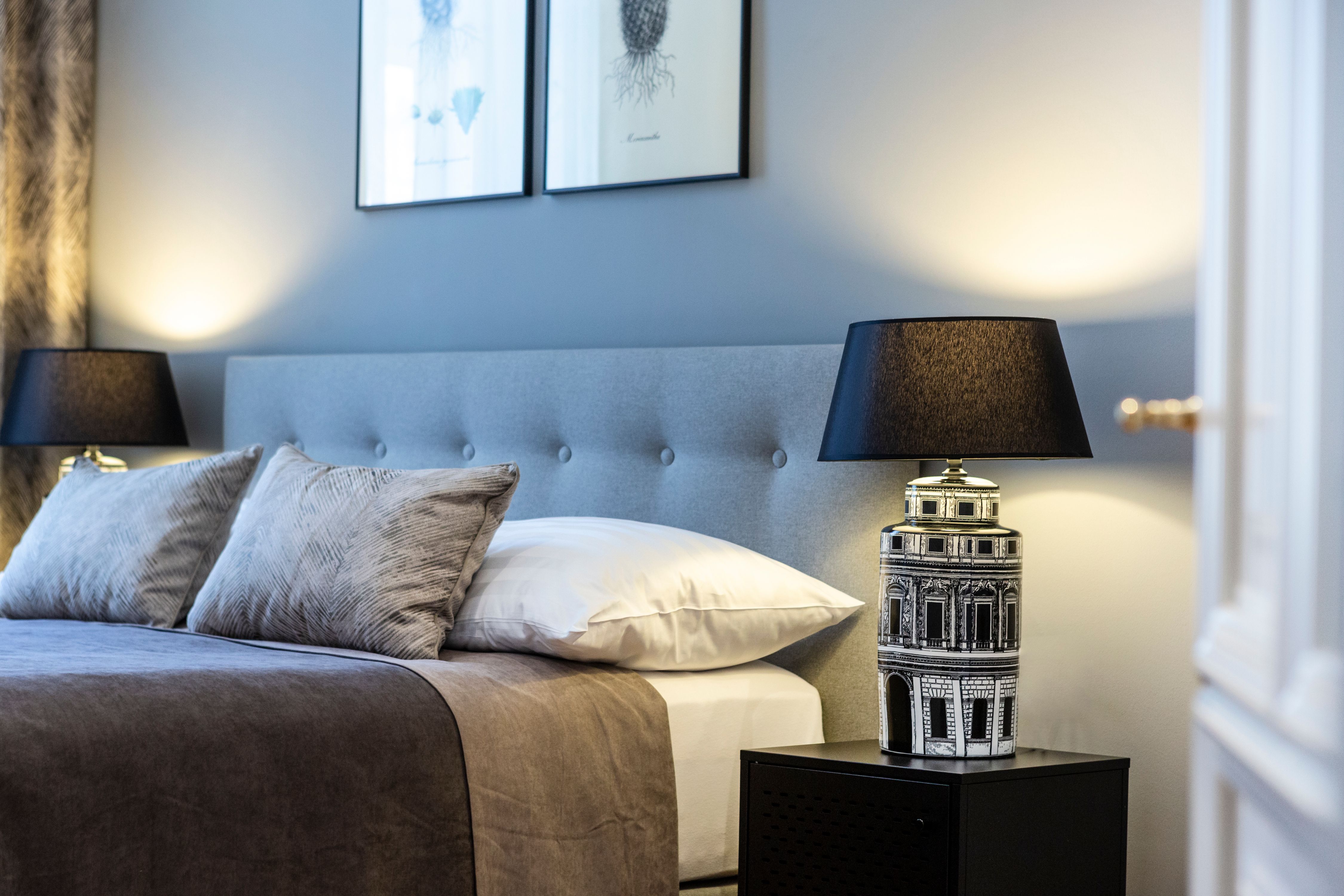 Elegantná dvojlôžková izba so sivým čelom, dvoma vankúšmi, nočnou lampou a nástennými obrazmi.