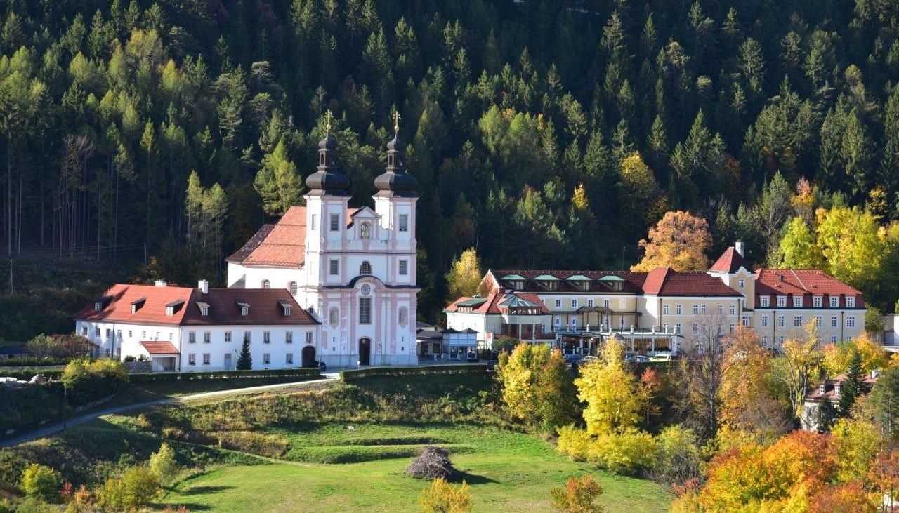 Pútnický kostol Maria Schutz pred zalesneným kopcom na jeseň.