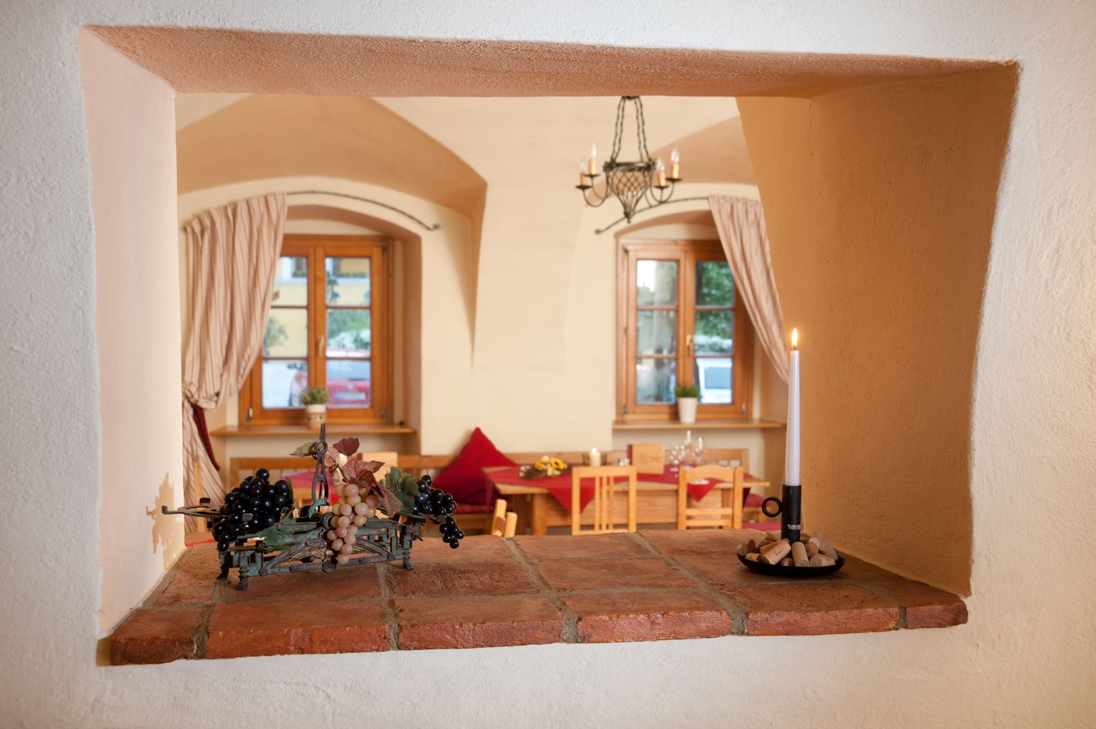 Pohľad cez otvor v stene do útulnej izby s dreveným nábytkom a svetlom sviečok.