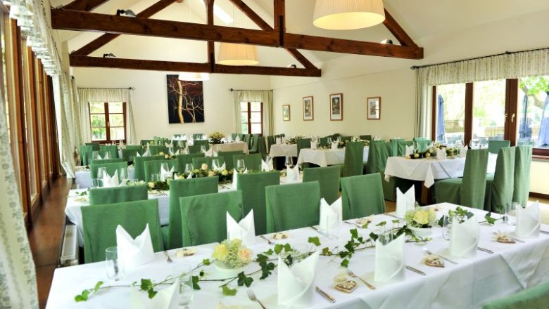 Pohľad do interi&eacute;ru sl&aacute;vnostne vyzdoben&eacute;ho hostinca so zelen&yacute;mi stoličkami a dreven&yacute;mi tr&aacute;mami.