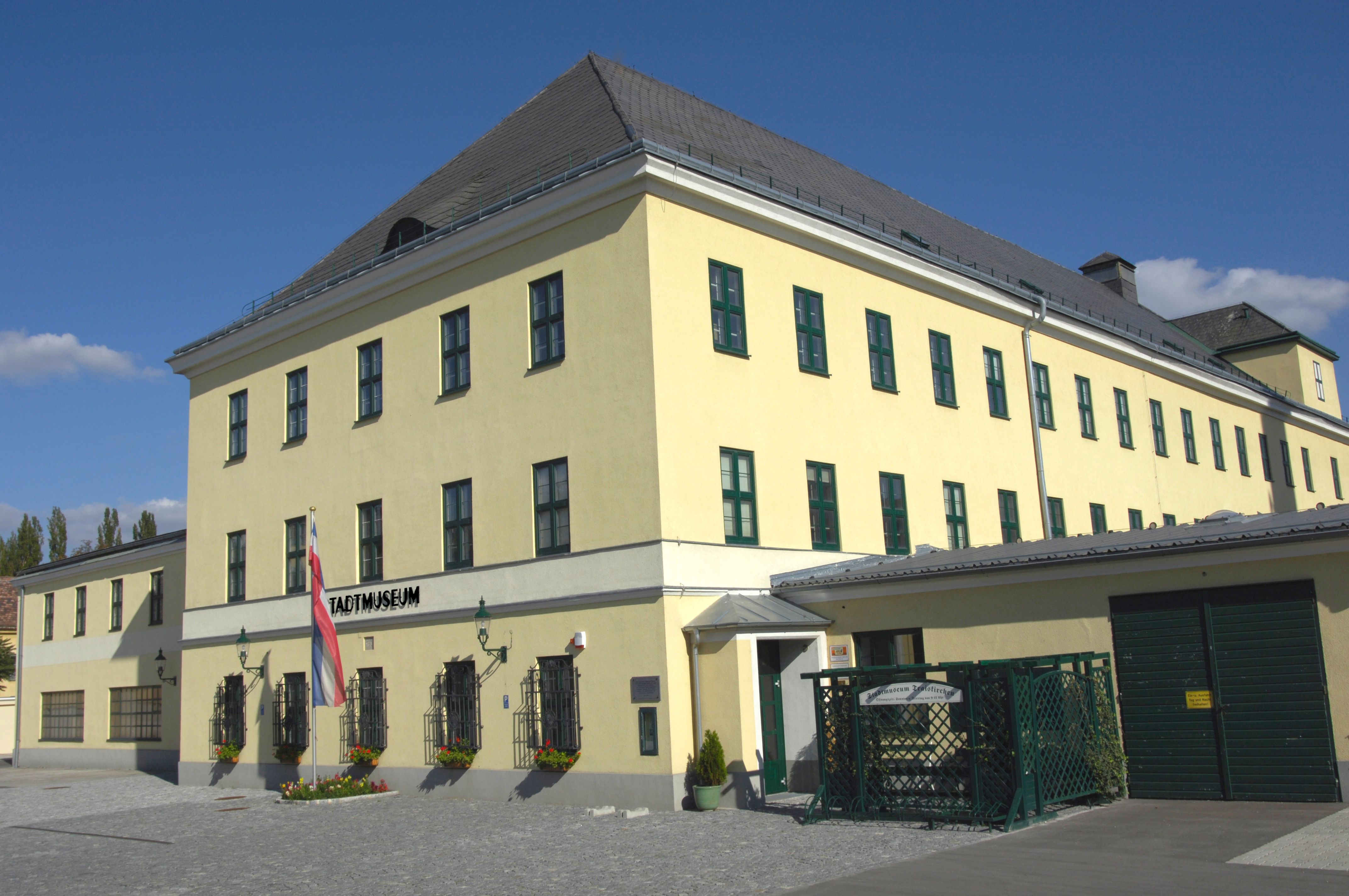 Žltá budova s nápisom "Stadtmuseum" a rakúskou vlajkou pred ňou.