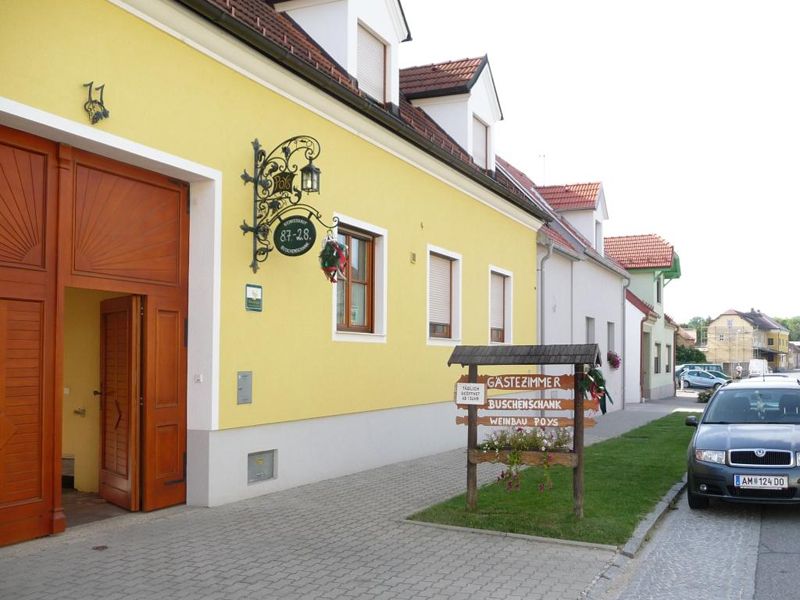 Žltá budova s nápisom "Gästezimmer vínne šenky Weinbau Poys" a zaparkované auto pred ňou.