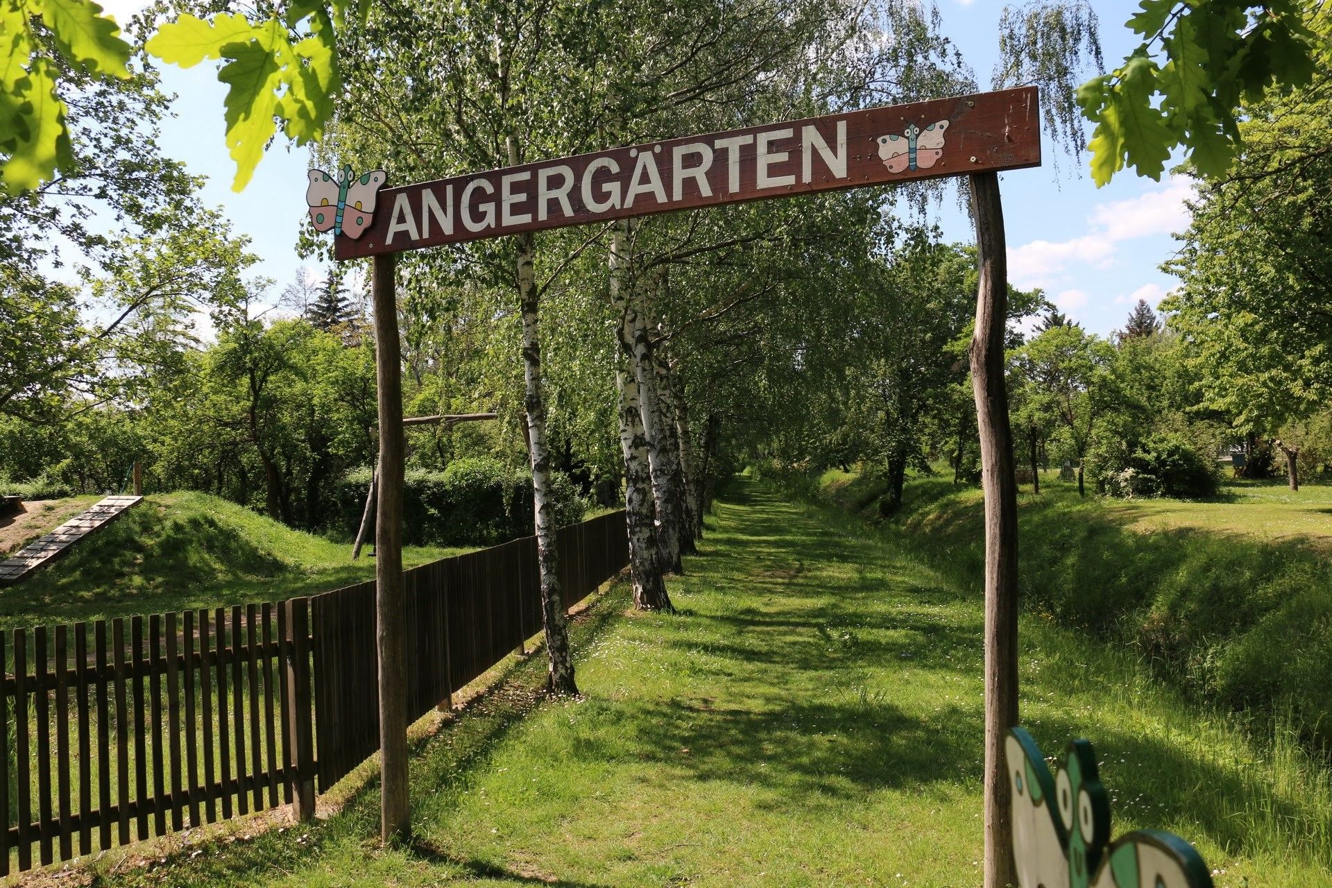 Vchod do Angergärten s drevenou tabuľou a stromami v pozadí.