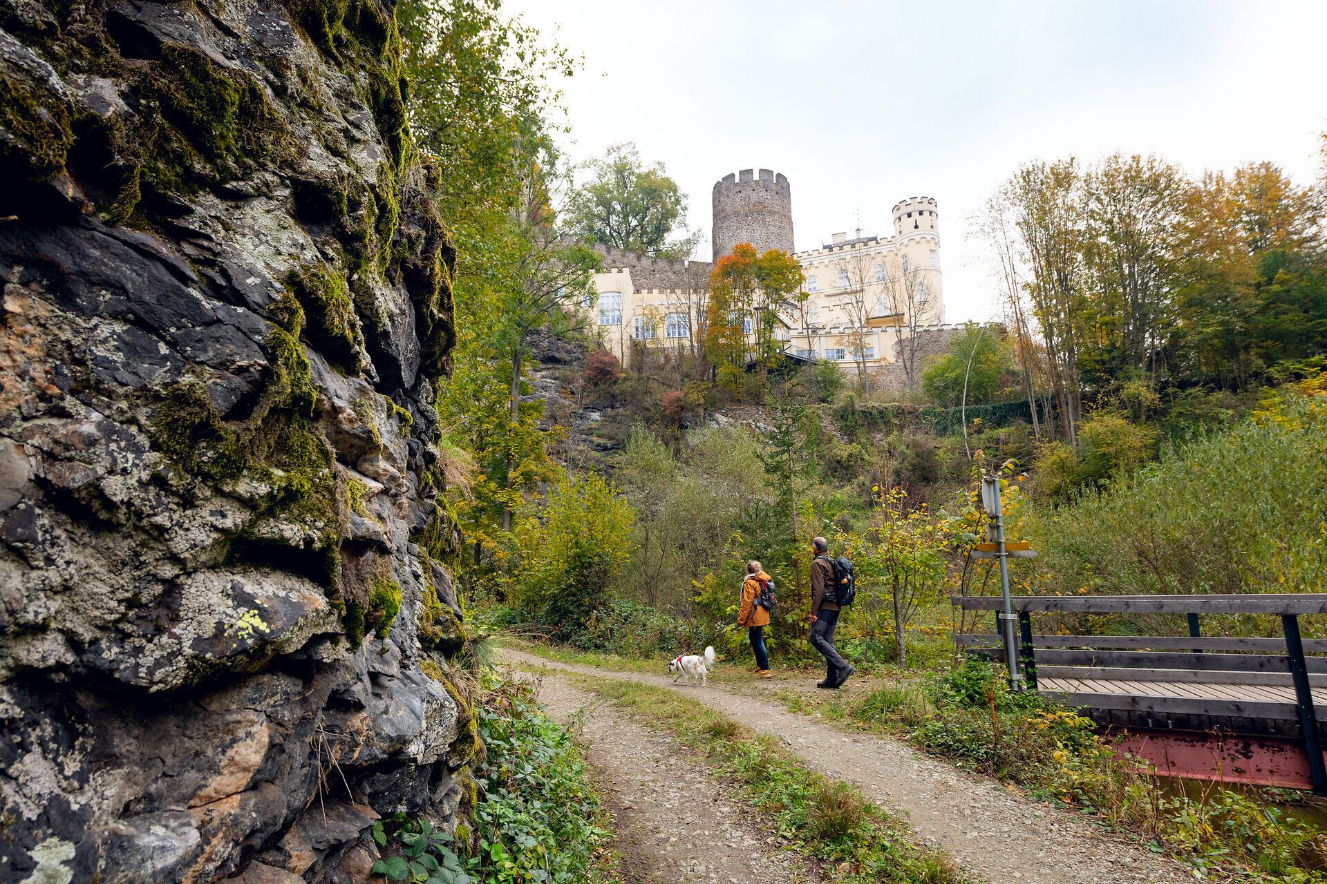Malebný turistický chodník vedie sviežou prírodou, obklopený farebným jesenným lístím a kopcami. V pozadí sa týči majestátny hrad Hartenstein, ktorý dodáva scenérii nádych histórie a romantiky. Ideálne miesto pre milovníkov prírody a histórie, ktorí si chcú vychutnať krásu krajiny.