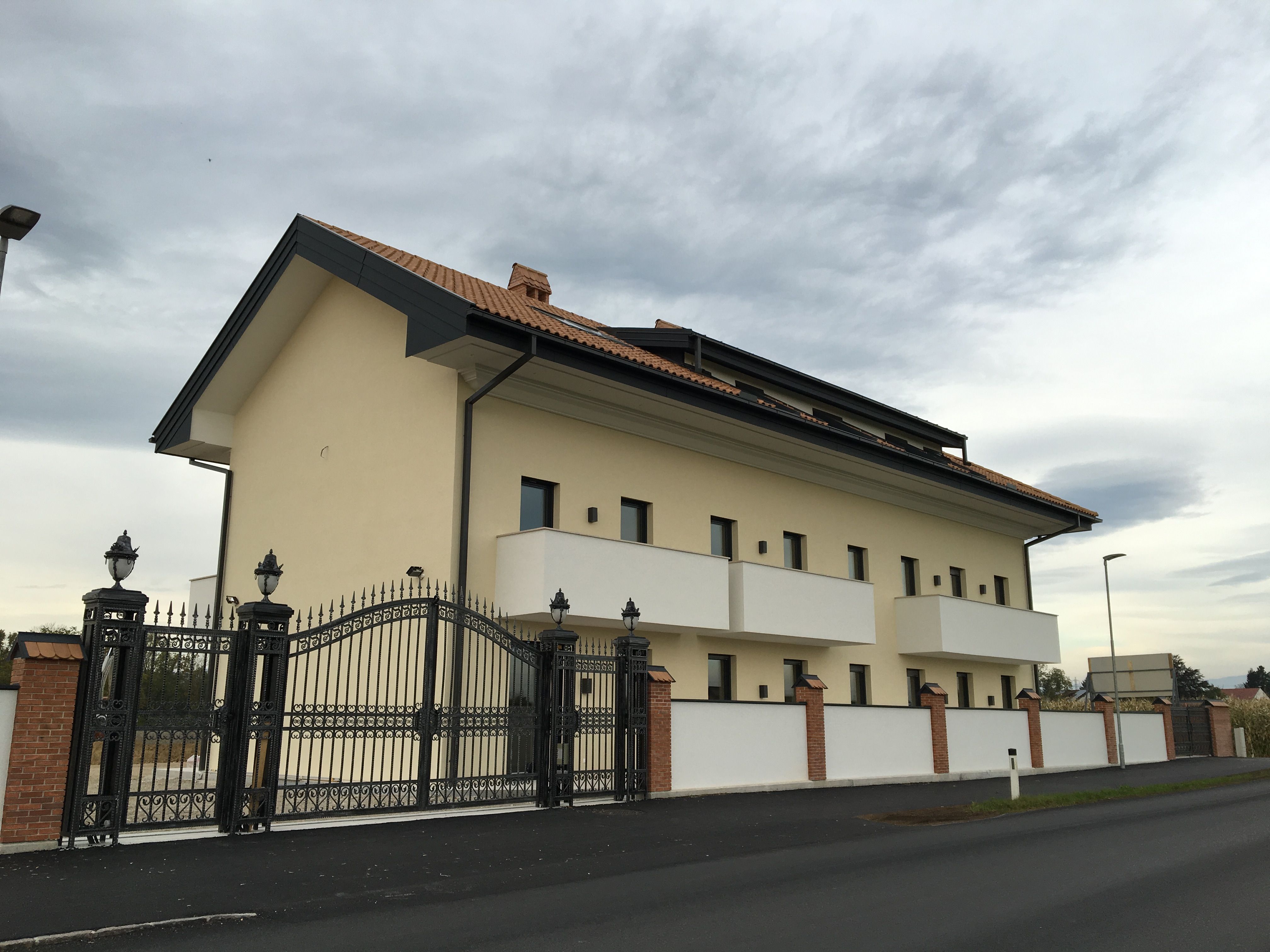 Pohľad zvonku na modernú budovu so škridlovou strechou a kovanou bránou.