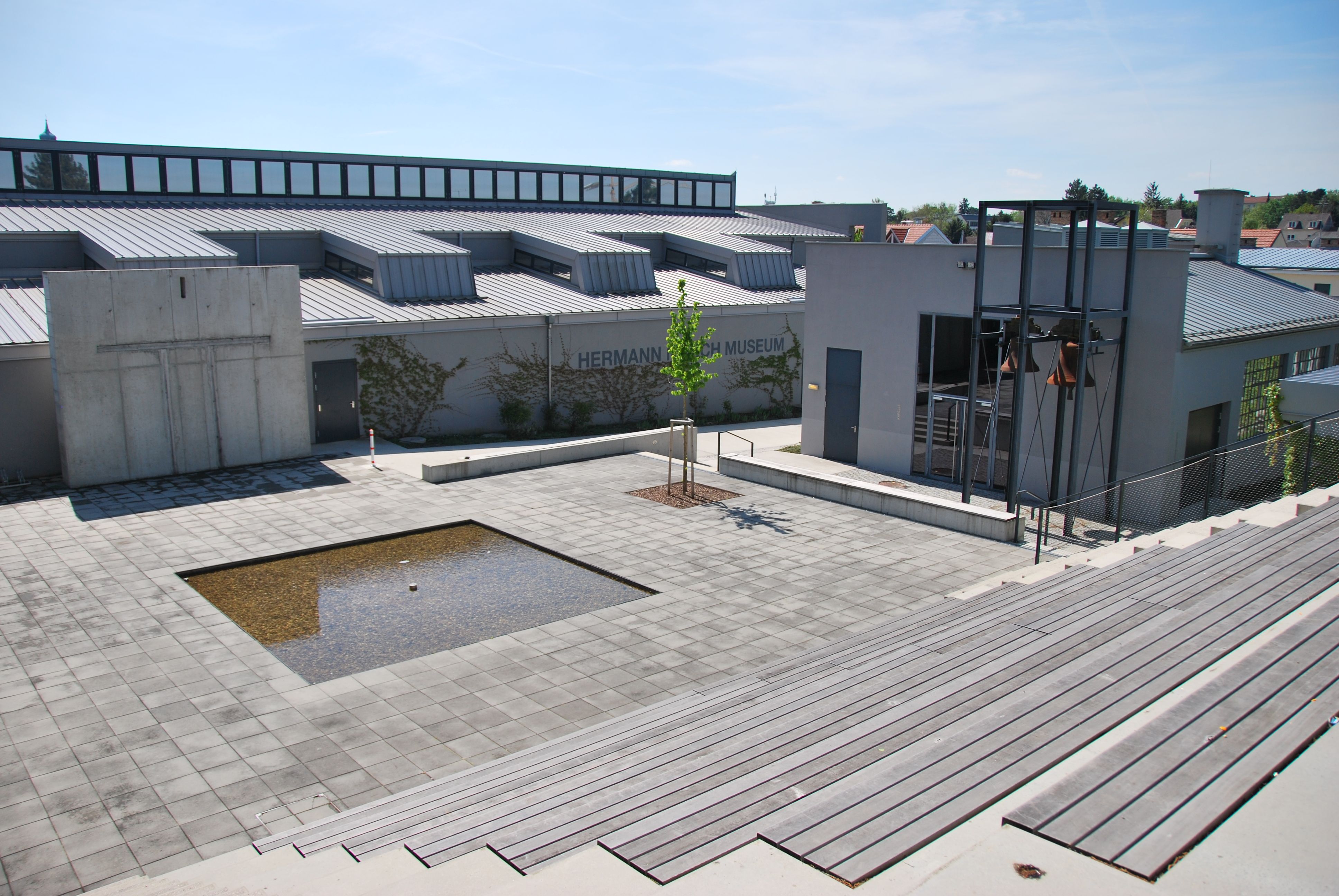 Exteriérový pohľad na Múzeum Hermanna Nitscha s moderným dizajnom a malou vodnou nádržou na námestí.