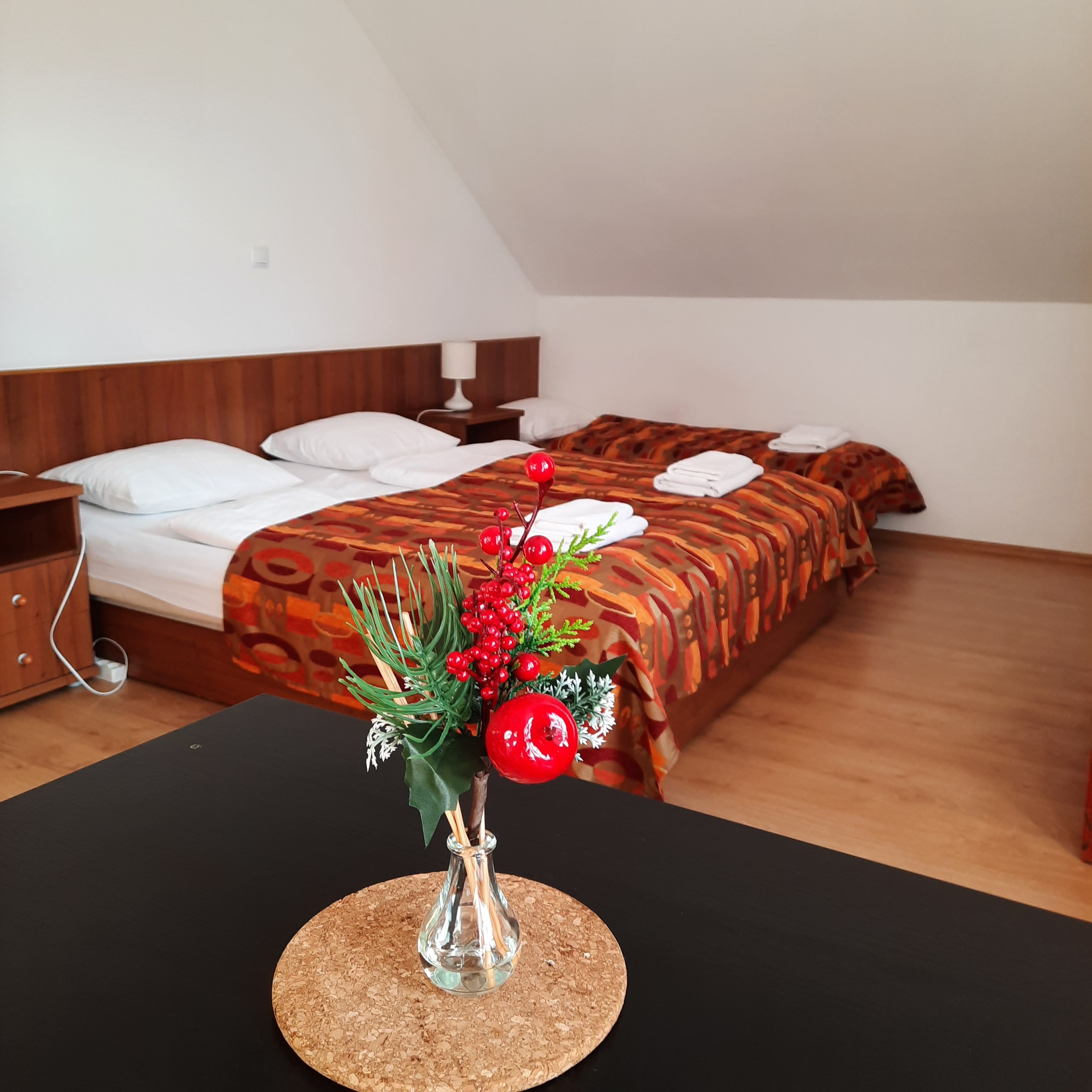 Útulná spálňa s dvoma posteľami, zdobená červenými bobuľami vo váze v popredí.