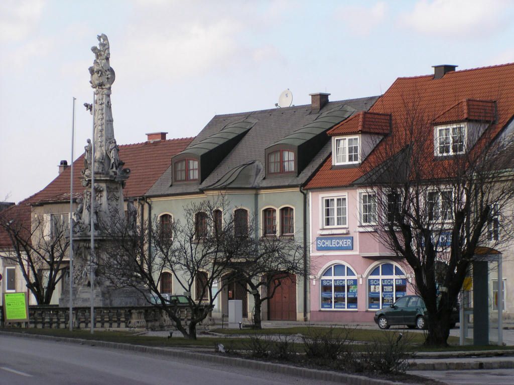 Scéna ulice v Ebenfurte s historickými budovami a sochou.