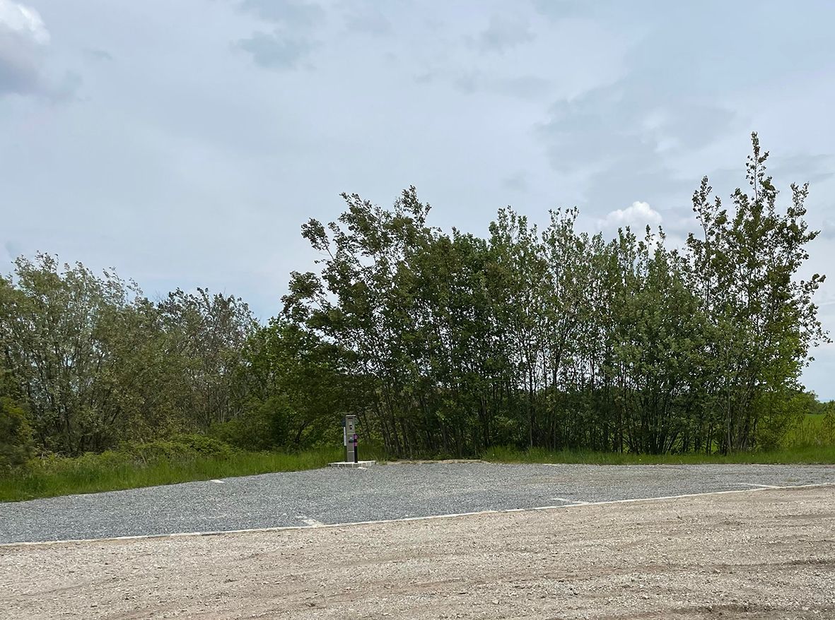 Prázdne miesto pre karavan so štrkovou podlahou, obklopené stromami a zamračenou oblohou.