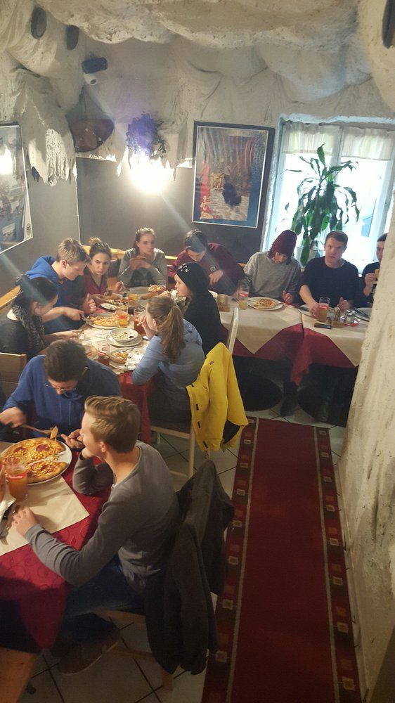Skupina ľudí jediacich pizzu v útulnej reštaurácii s jaskynnými stenami.