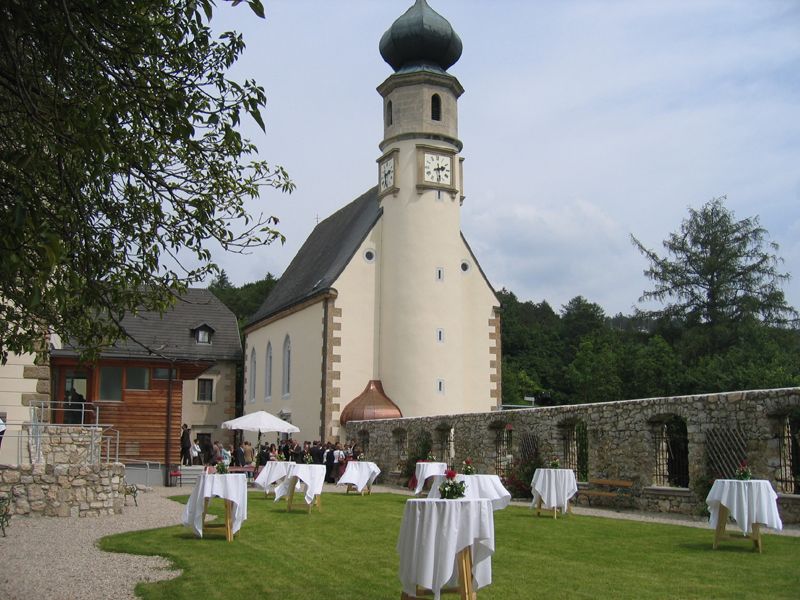 Kostol s vežou a záhrada s barovými stolmi, svadobná scéna.