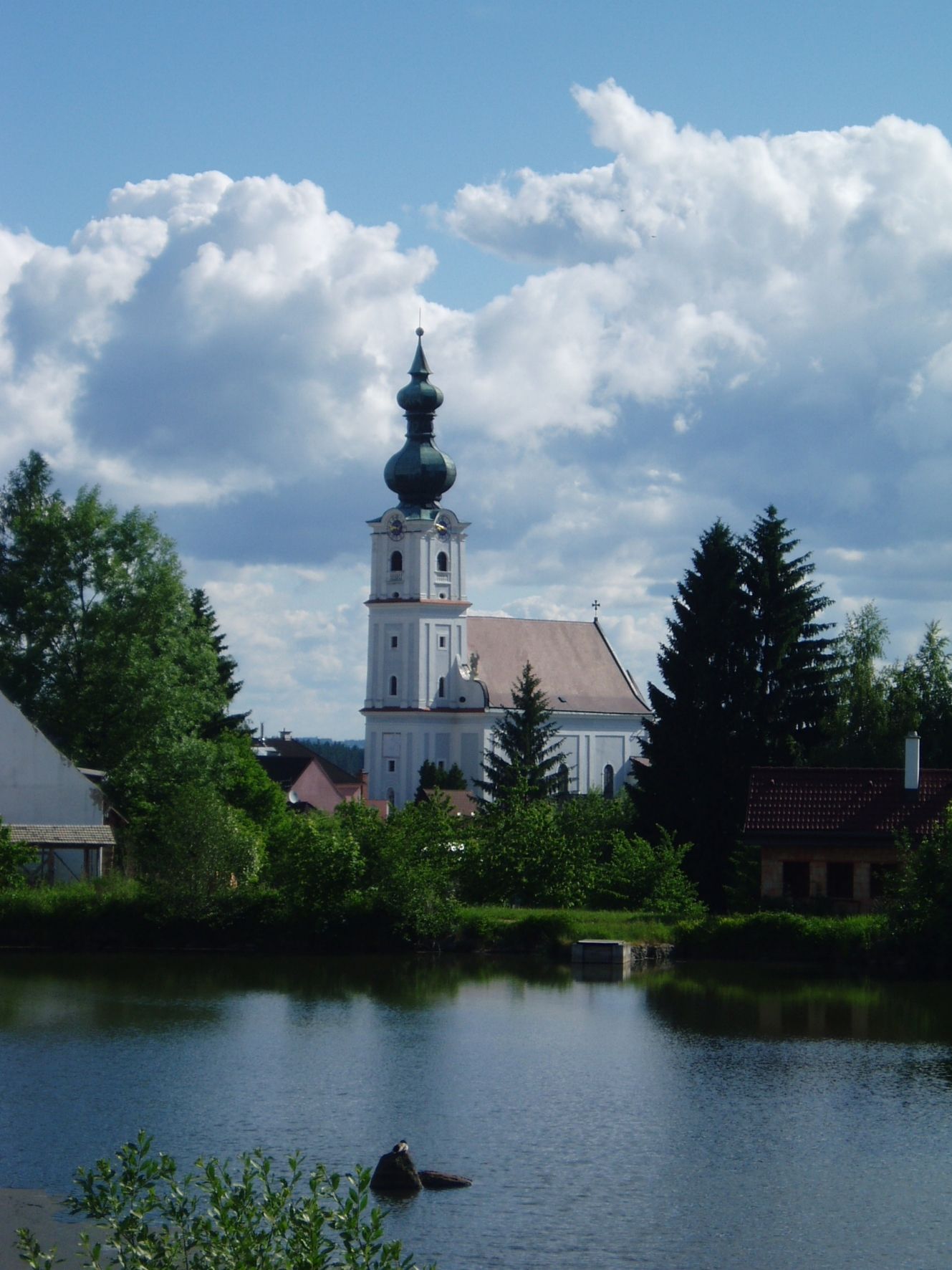 Kostol v Kirchbergu am Walde s rybníkom v popredí a zamračenou oblohou.