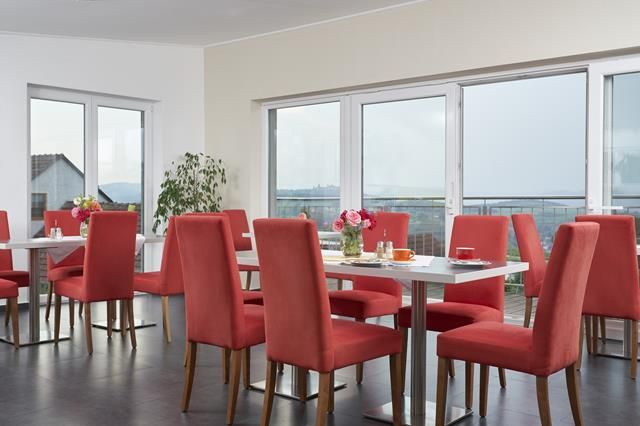 Raňajková miestnosť s červenými stoličkami, dreveným nábytkom a kávovarom.