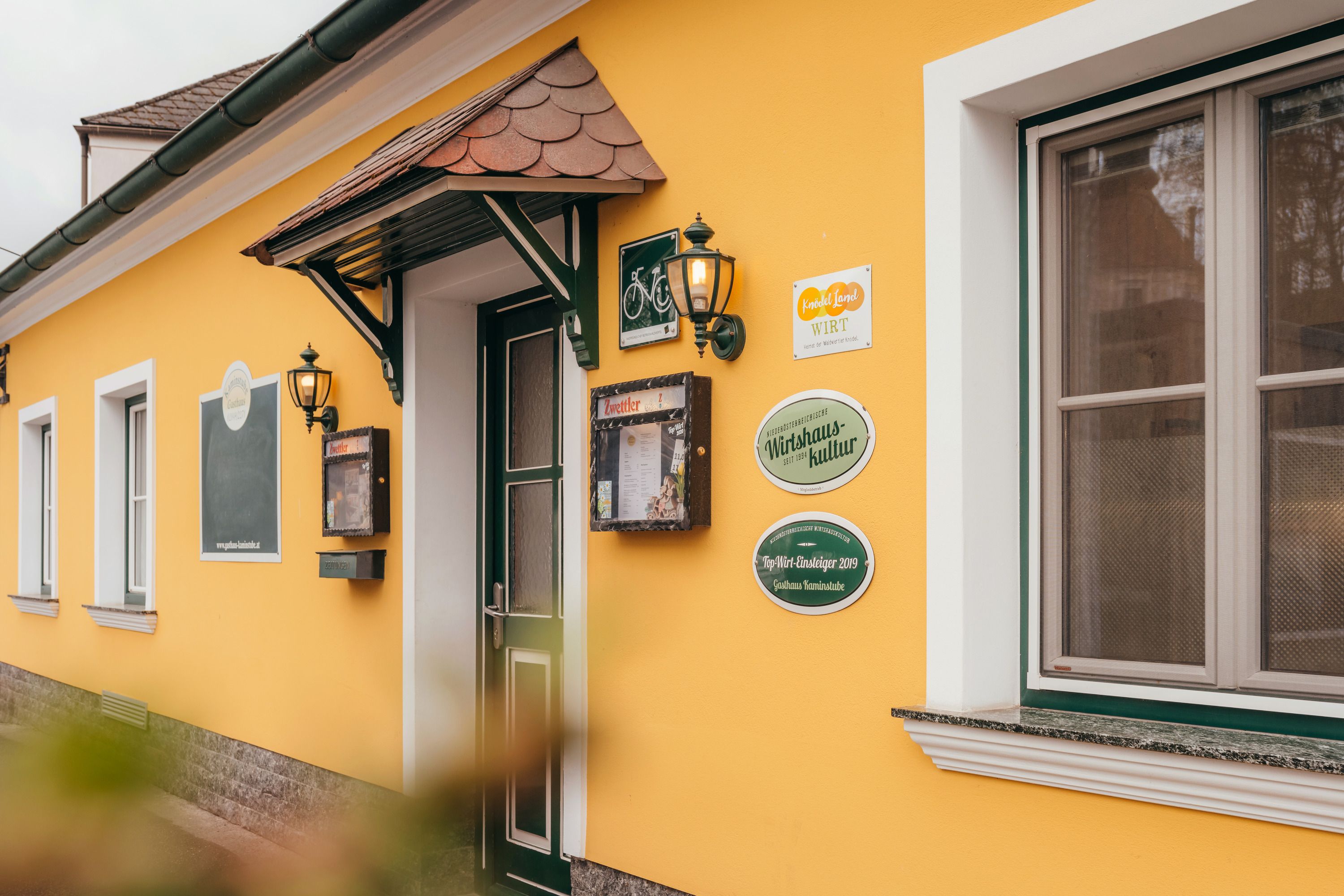 Žltá budova s dverami a oknami, nápismi a lampášmi na stene.