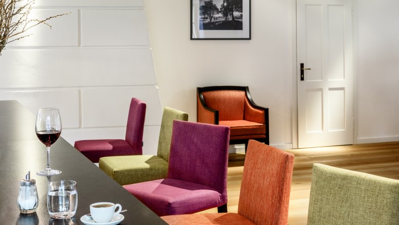 Pohľad do interiéru moderného hotelového salónika s farebnými stoličkami, stolom s nápojmi a obrazom na stene.